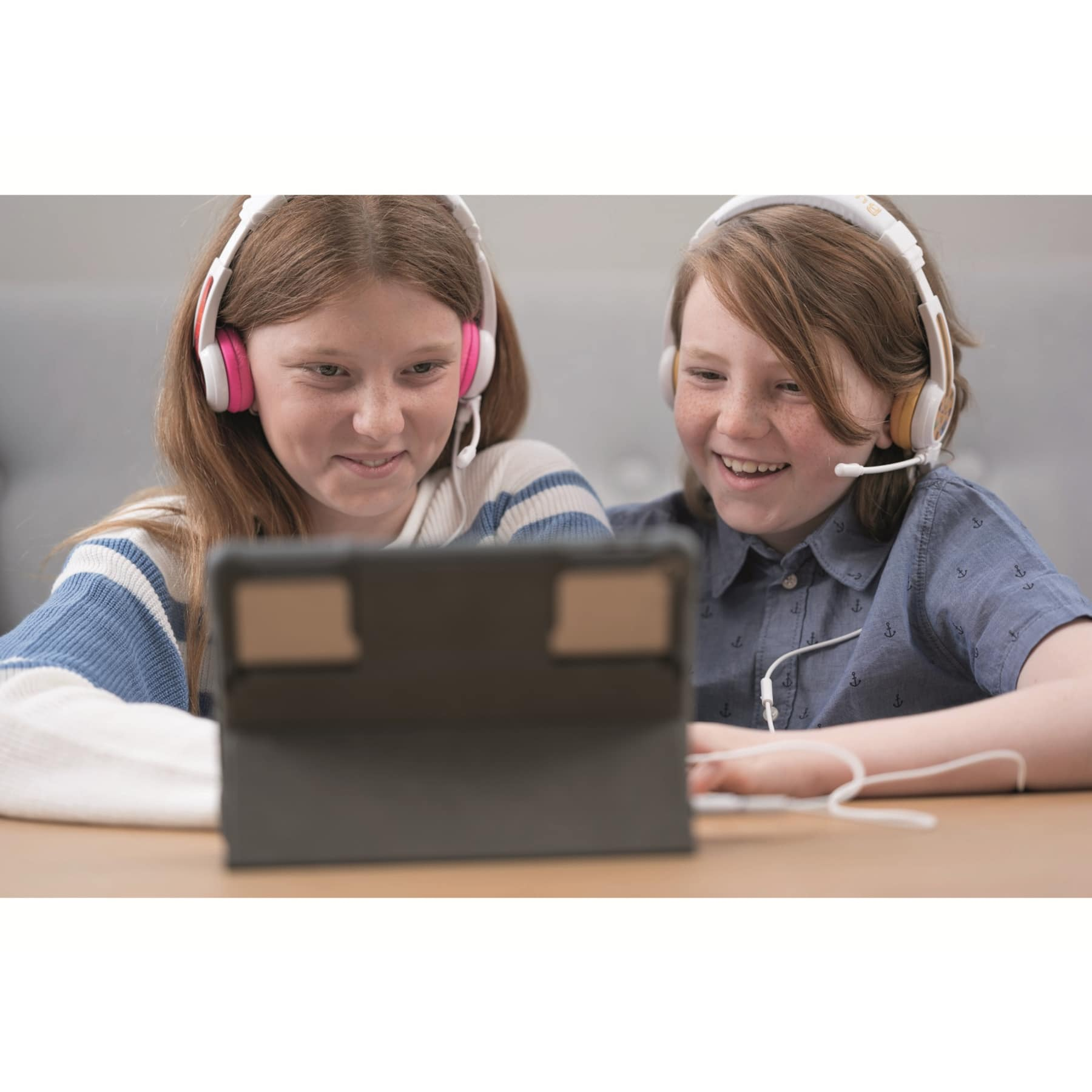 Deux enfants portant des écouteurs, regardant une tablette. L'un sourit.