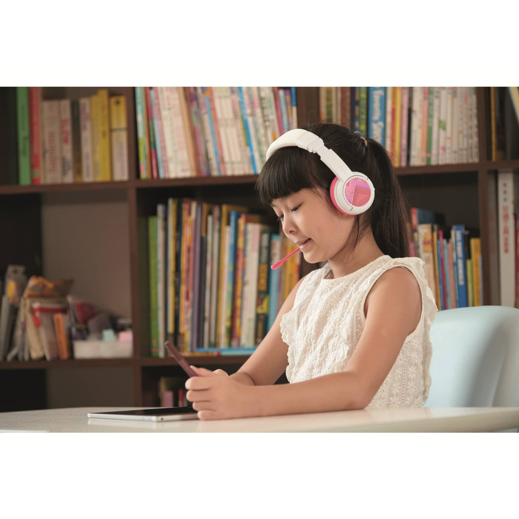 Ragazza con cuffie bianche e rosa, tiene il telefono, legge su un tablet.