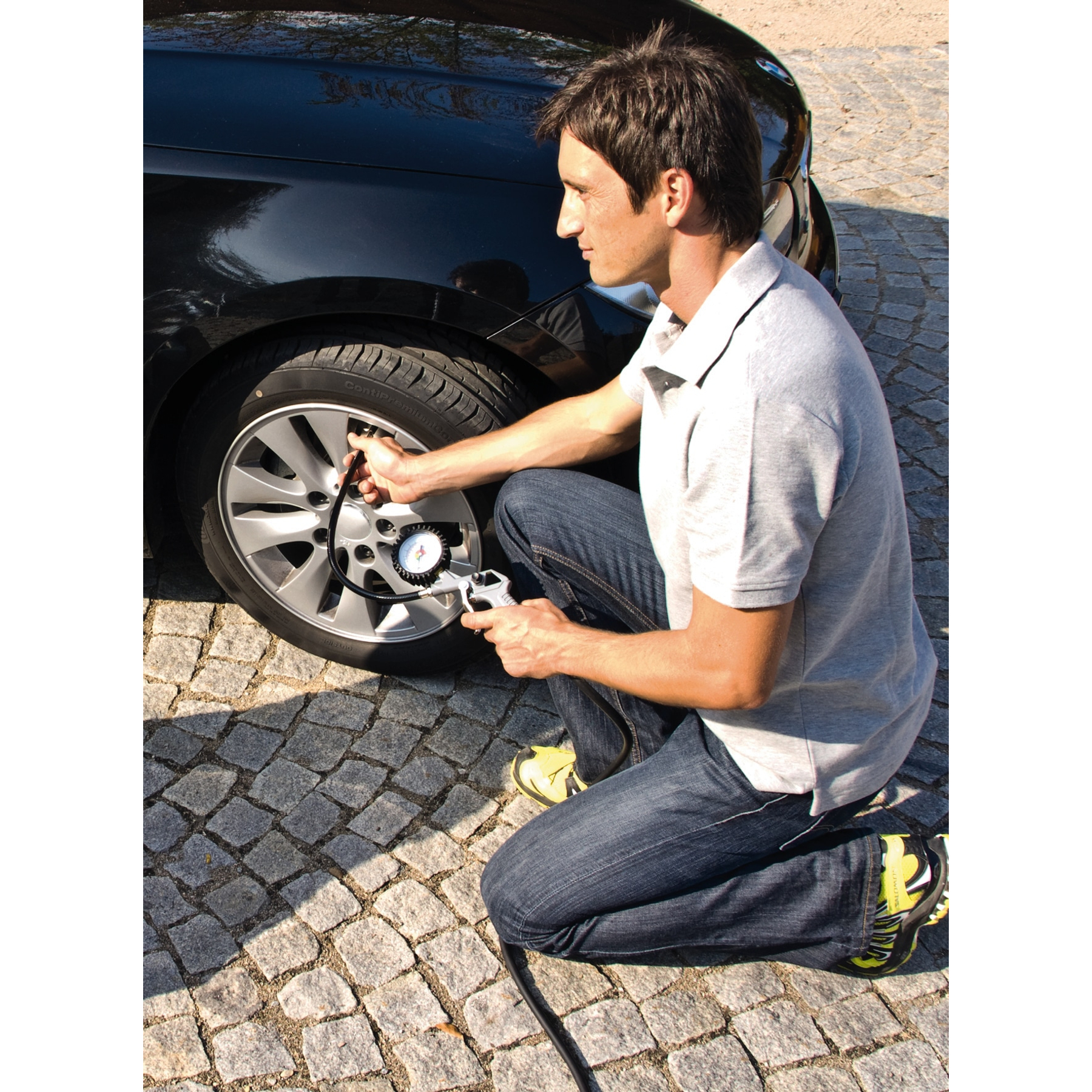 Ein Mann, der einen Autoreifen mit einem Messgerät auf einer Pflasteroberfläche anpumpt, mit einem schwarzen Auto.
