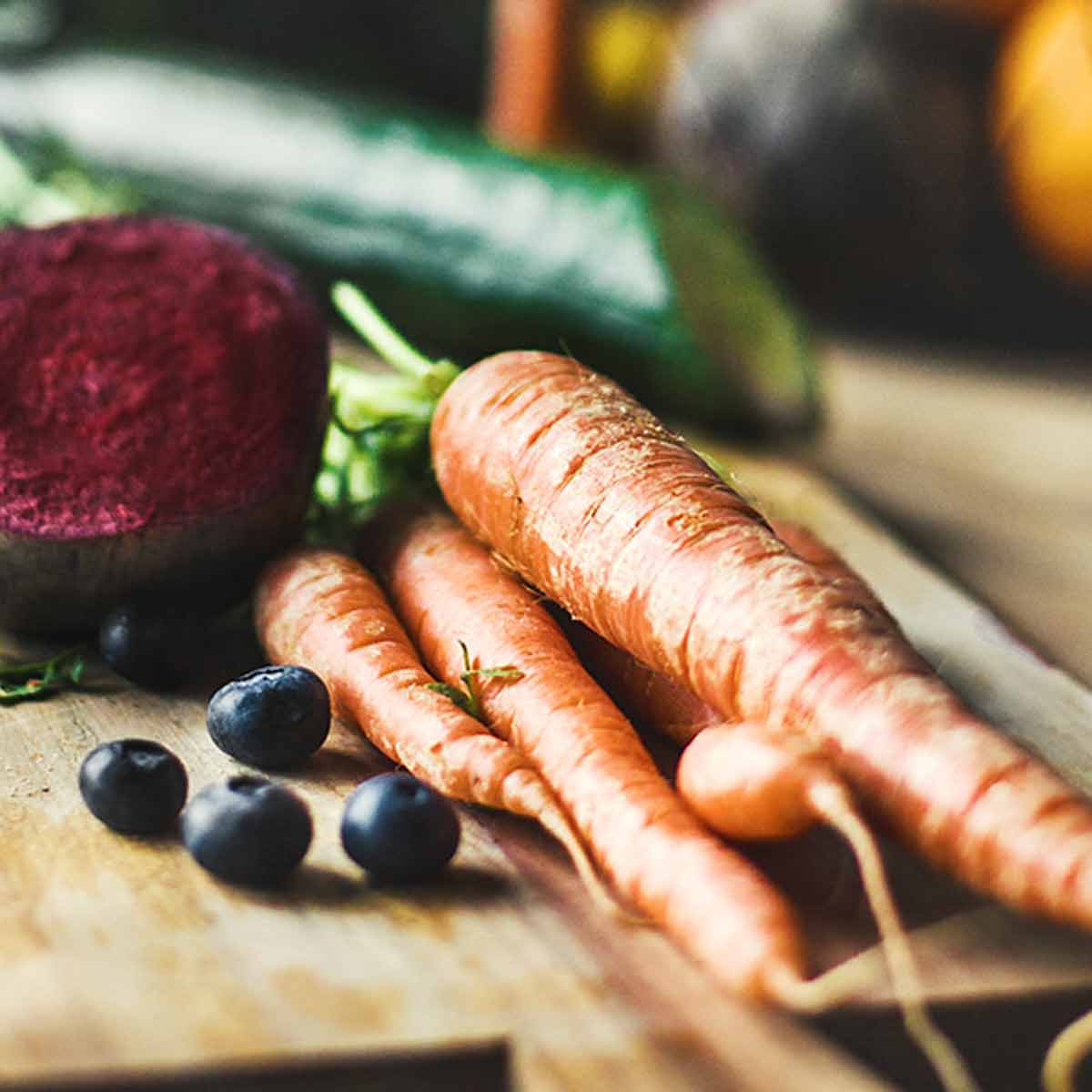Primo piano di verdure su un tagliere di legno: carote, mirtilli e barbabietola. Sfondo sfocato.