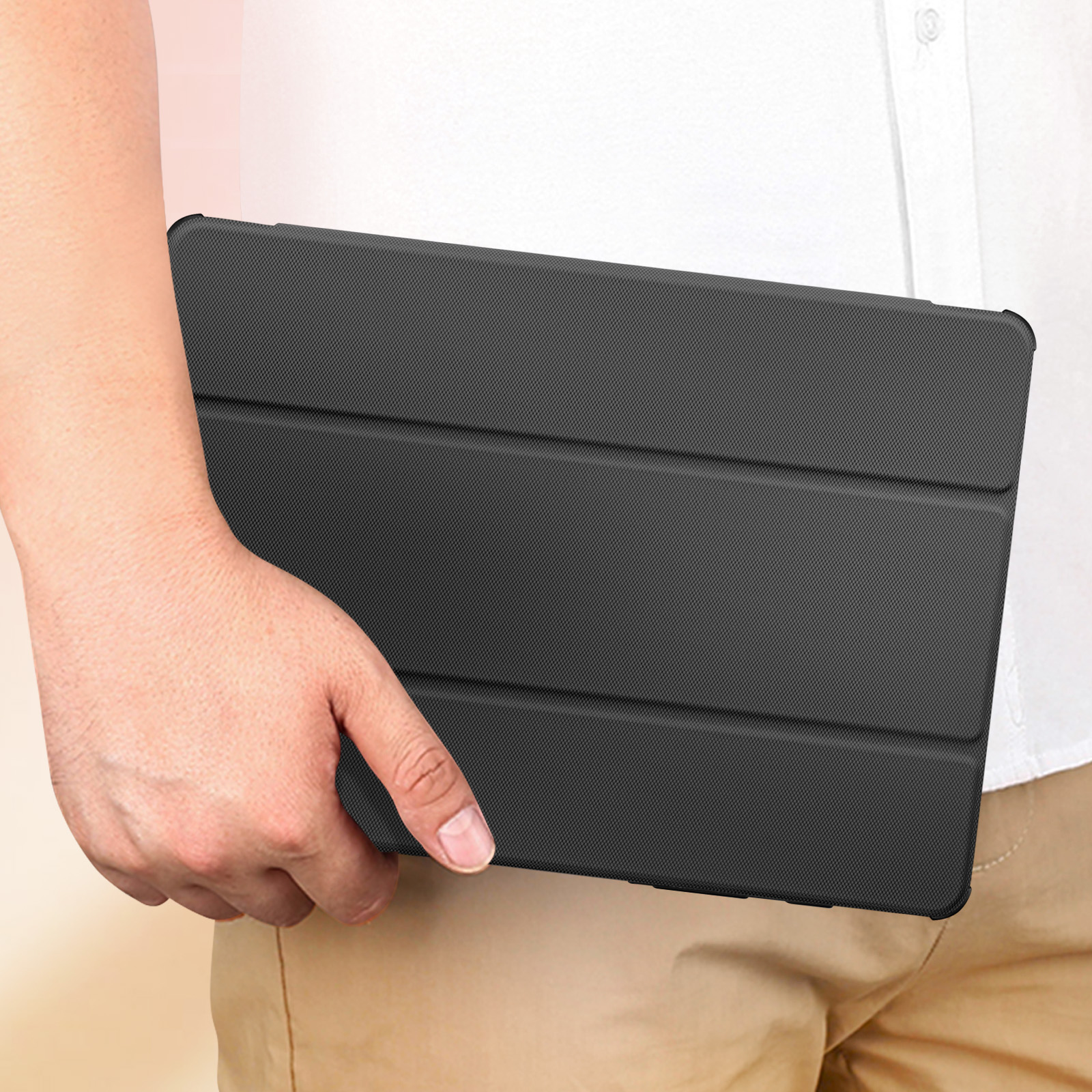 Una persona tiene in mano una custodia nera chiusa per tablet. La custodia ha una superficie strutturata. La persona indossa una camicia bianca.