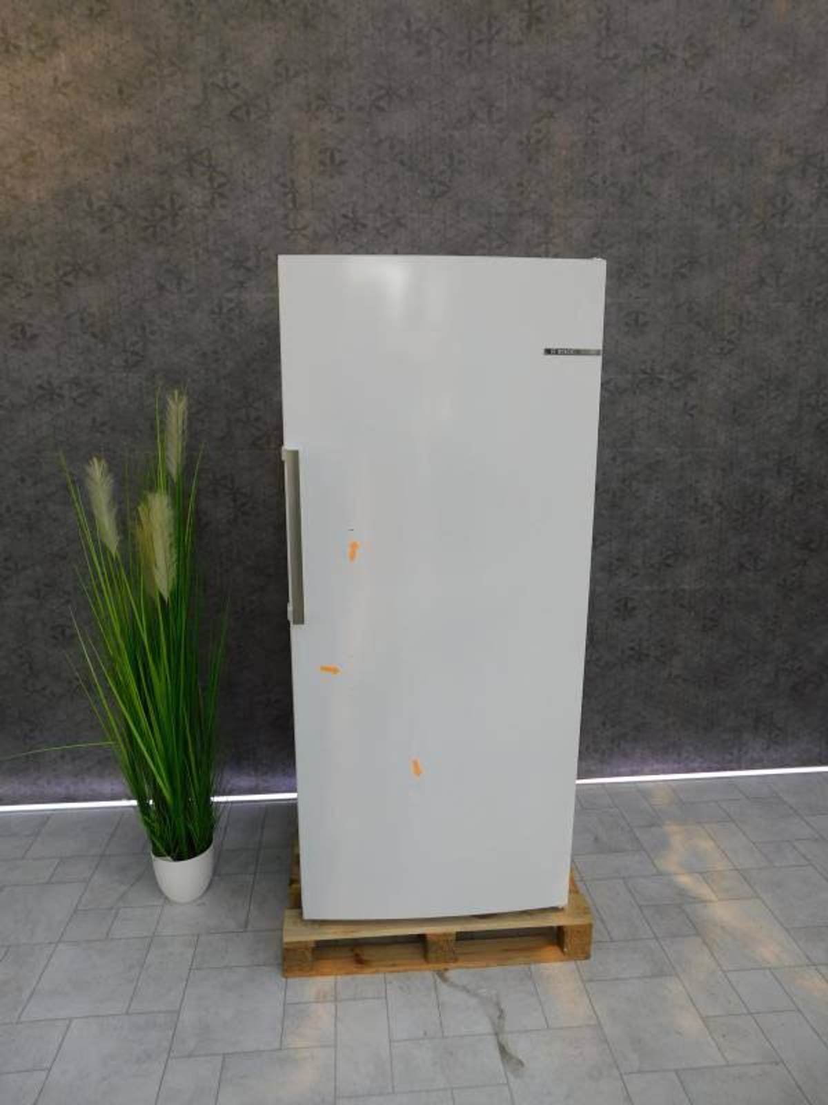 Biała lodówka stojąca na drewnianej palecie.