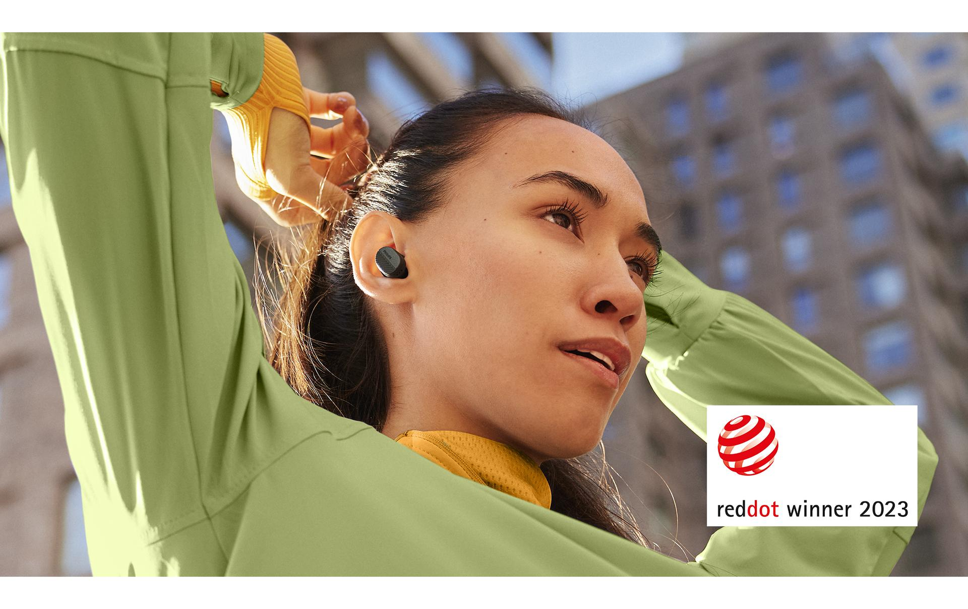 Kobieta nosząca słuchawki, Red Dot Winner 2023, na tle miasta.