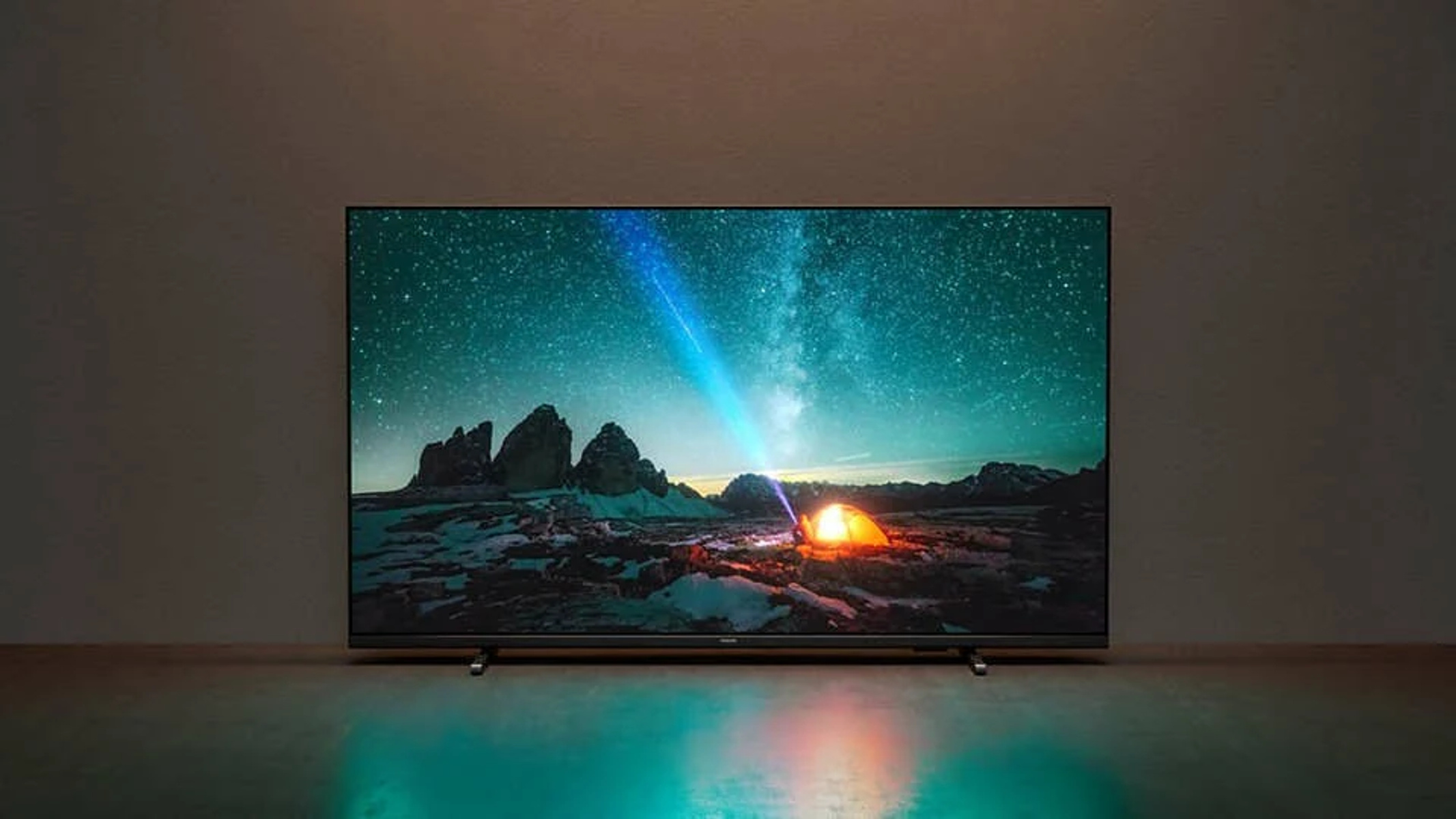 Duży telewizor wyświetla scenę rozgwieżdżonej nocy z namiotem i światłem. Jest w słabo oświetlonym pokoju.