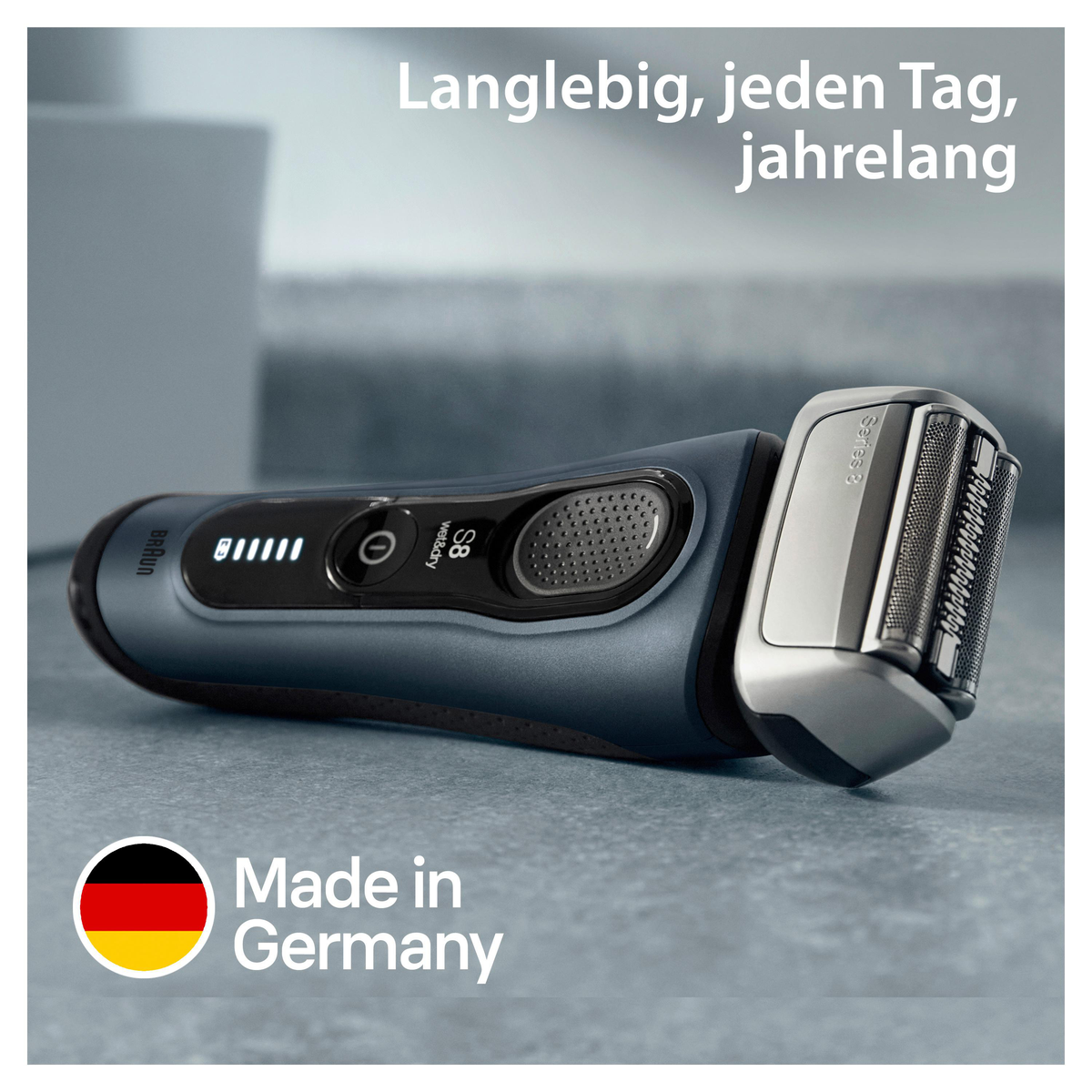 Ein schwarzer und grauer Elektrorasierer auf einer grauen Oberfläche, mit einer deutschen Flagge in der Ecke.