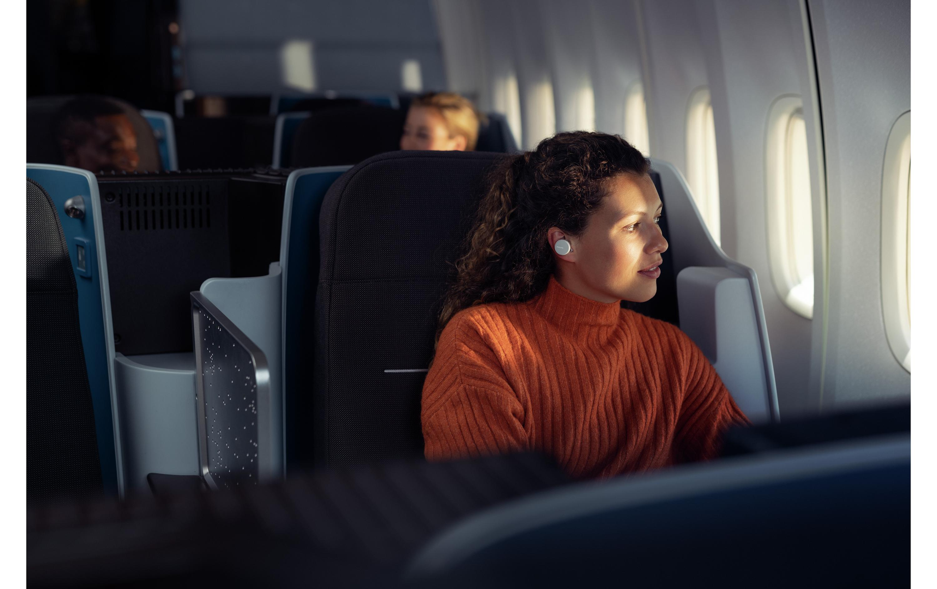 Eine Frau mit Ohrhörern im Flugzeug, die aus dem Fenster schaut.