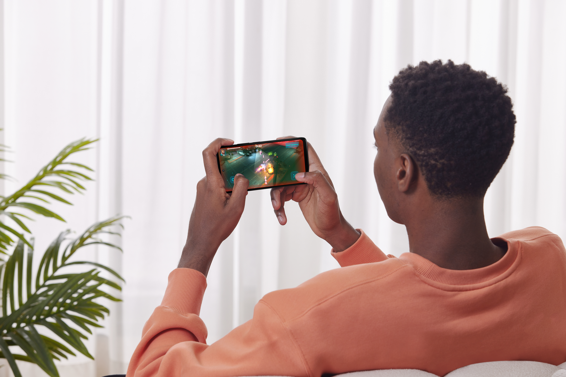 Un uomo tiene in mano un telefono, sta giocando. Lo schermo mostra una scena di gioco con azione.