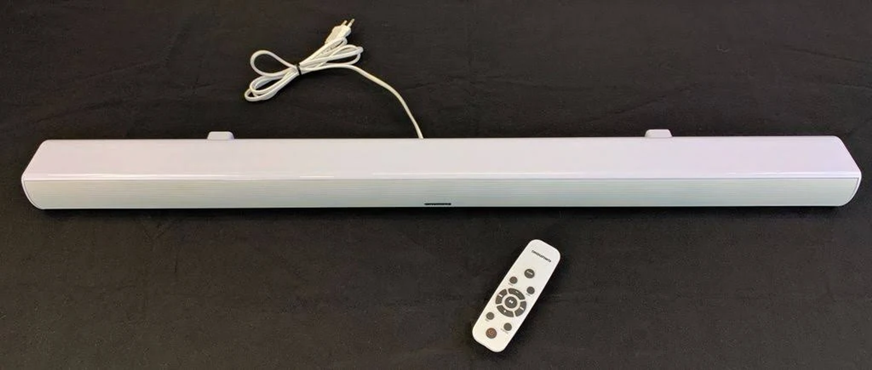 Biały soundbar z pilotem na czarnej powierzchni.