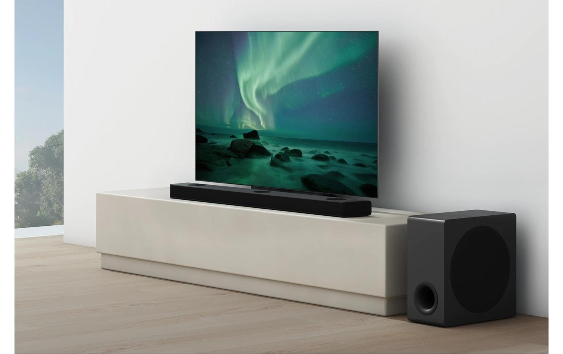 Ein Fernsehbildschirm mit einem Nordlichtbild, eine Soundbar und ein Subwoofer auf einem weißen Ständer.