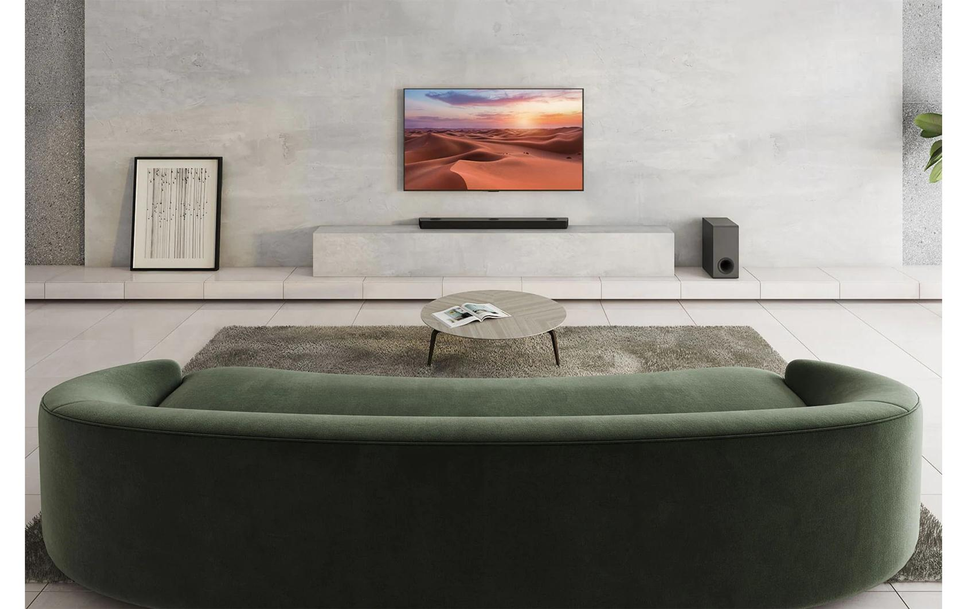 Wohnzimmer mit geschwungenem grünen Sofa, Fernseher und Teppich.