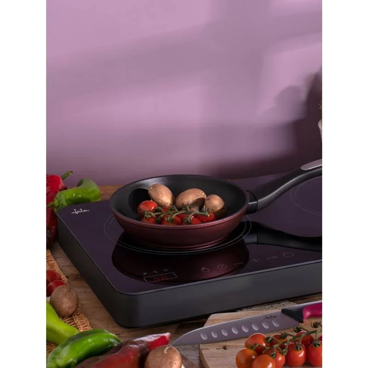 Una sartén en una placa de cocina con tomates y champiñones. Verduras en los lados.