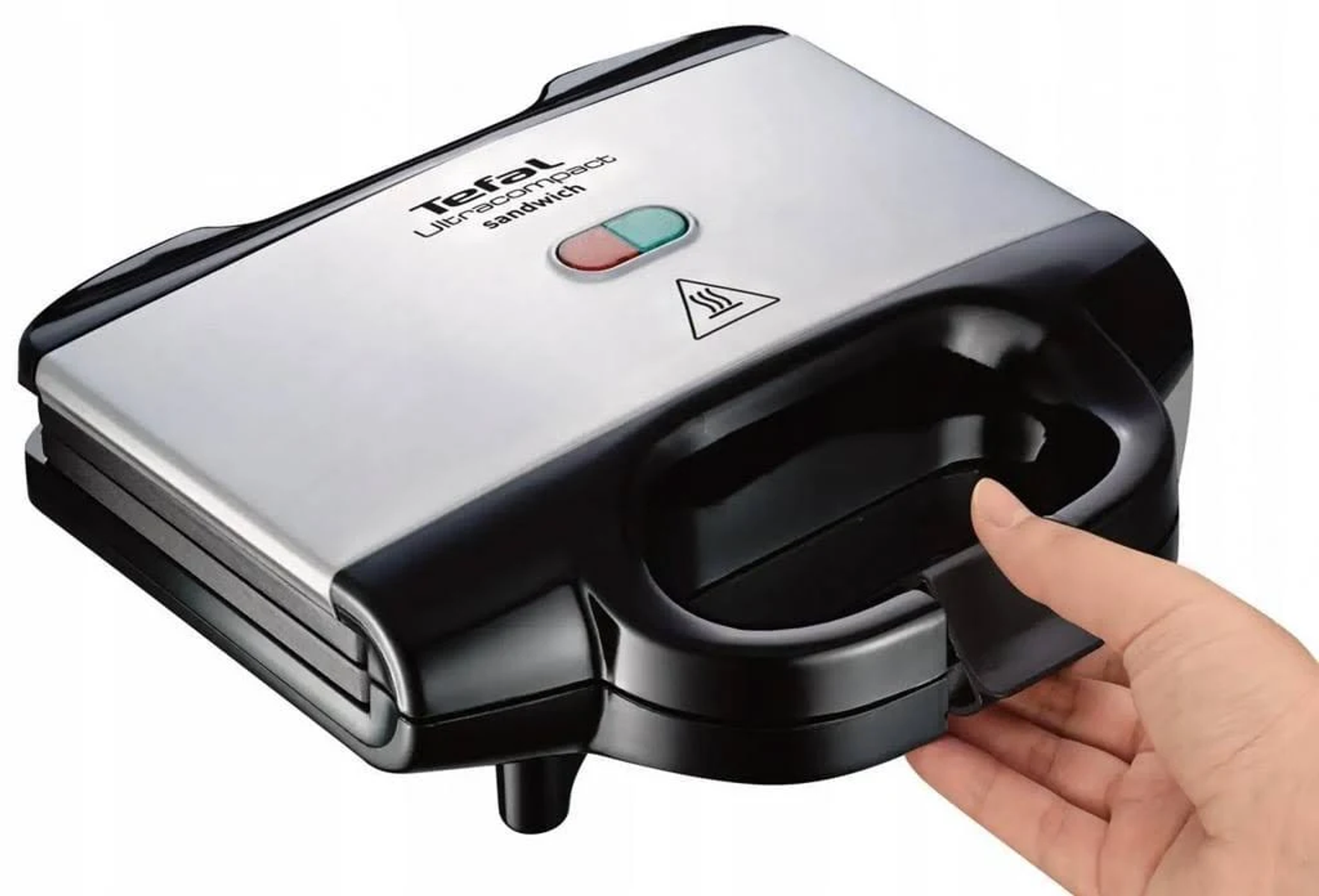 Srebrno-czarny opiekacz do kanapek z ręką otwierającą go. Widoczne czerwone i zielone światła.