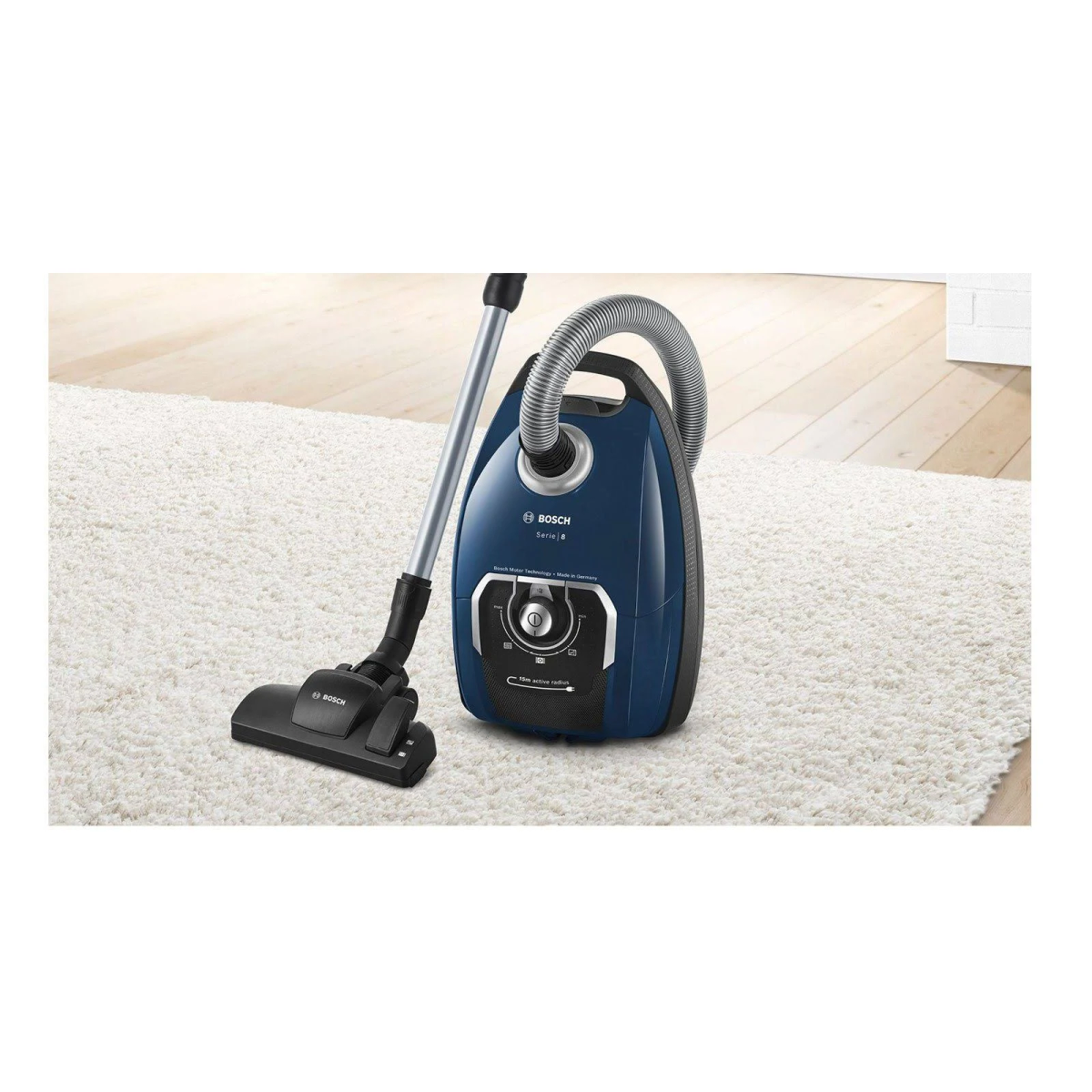 Niebieski odkurzacz na białym dywanie, ze srebrnym przedłużeniem i wężem.