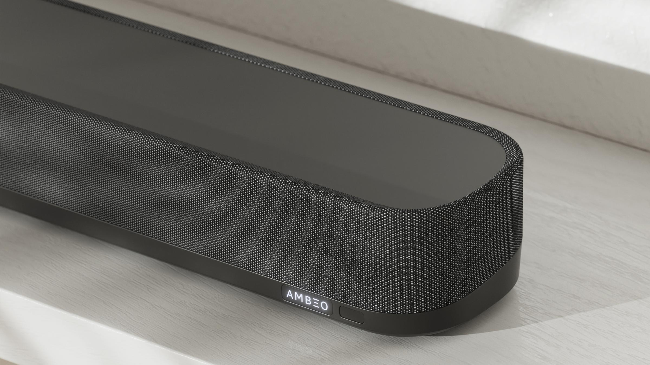 Eine schwarze Soundbar liegt auf einer weißen Oberfläche. Das Wort AMBEO steht auf der Soundbar.
