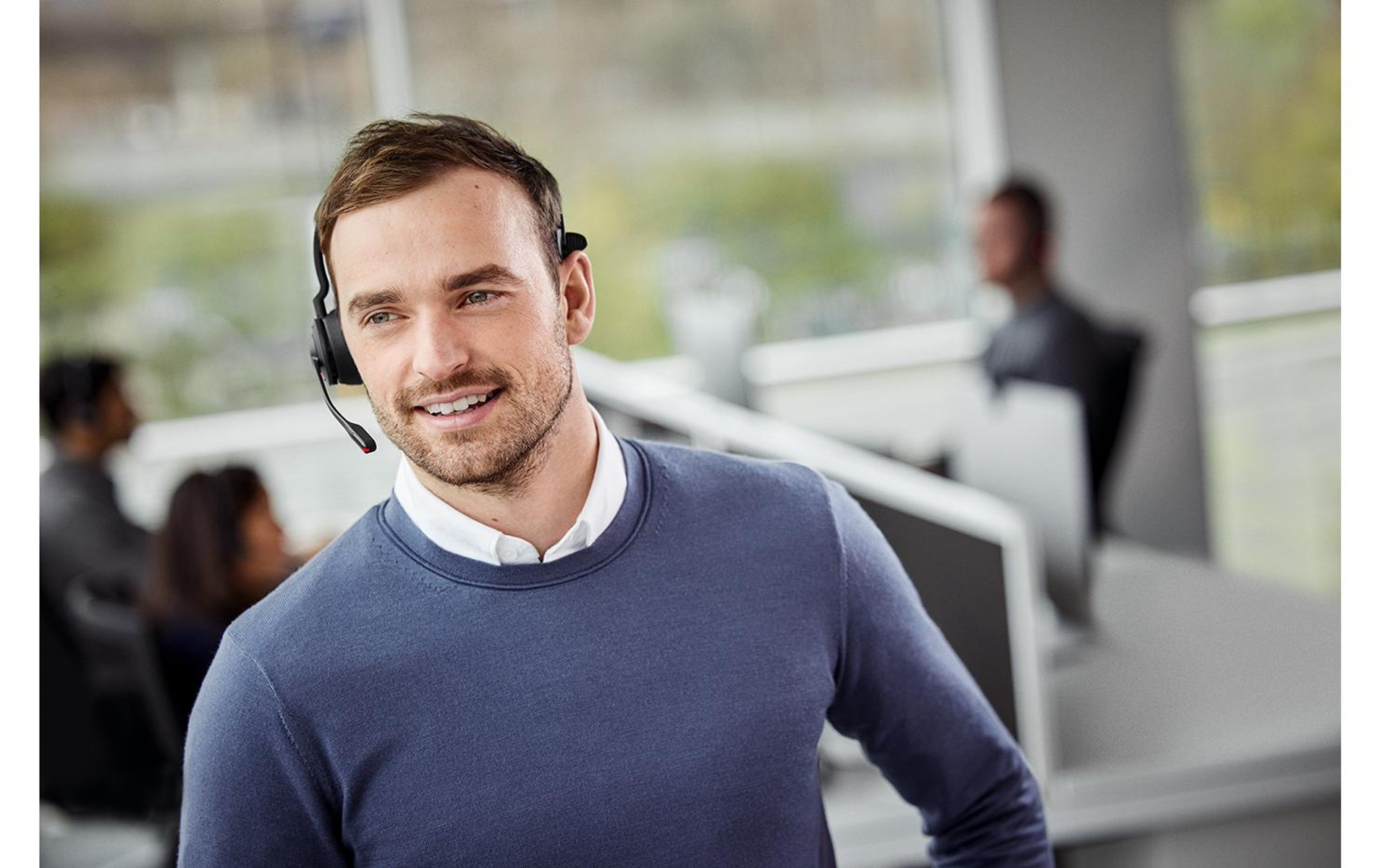 Mann mit Headset lächelt in einer Büroumgebung.