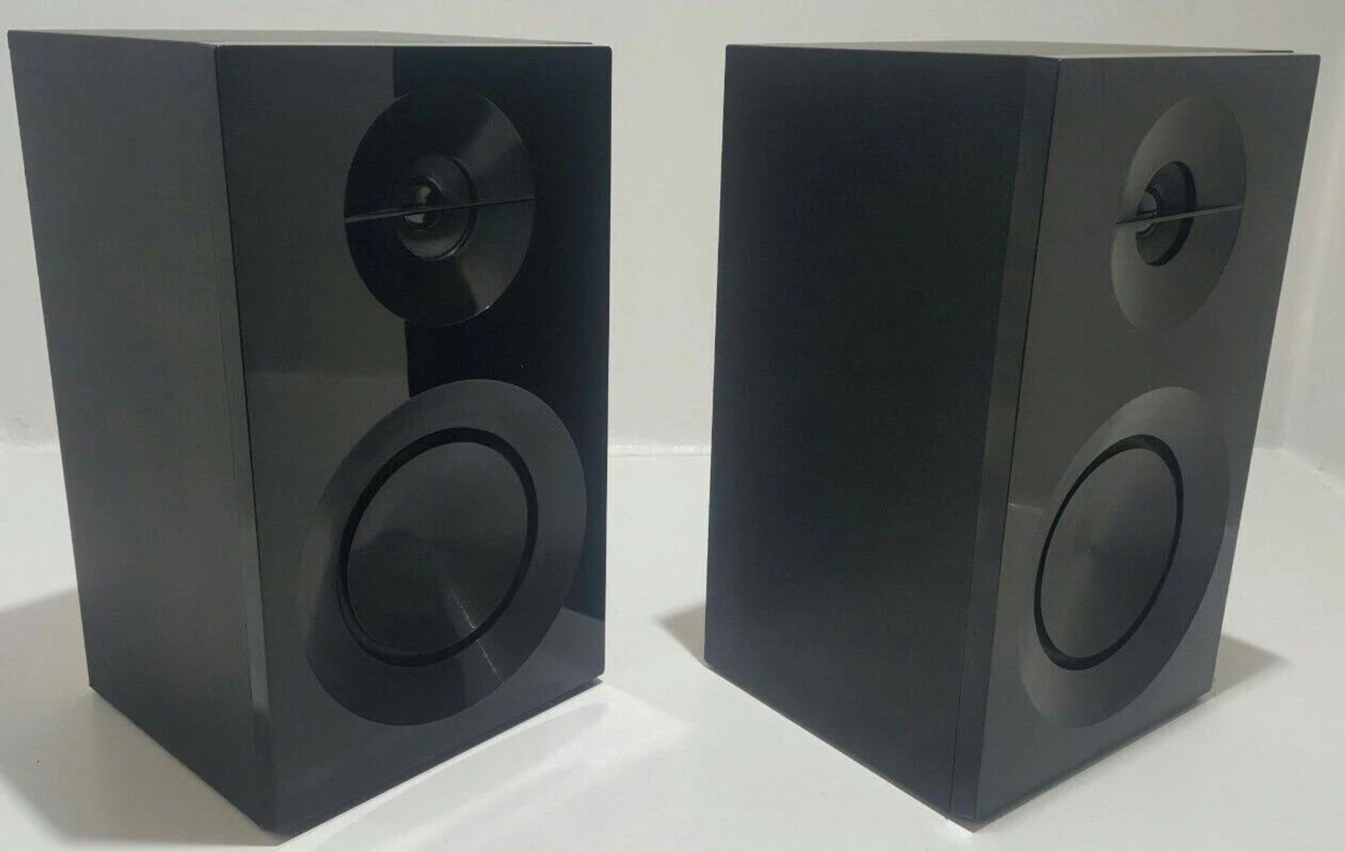 Dos altavoces negros brillantes, de pie, con elementos de altavoz circulares.