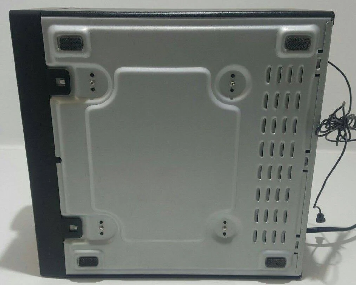Parte inferior de un dispositivo negro con orificios de ventilación y patas de goma. Varios tornillos son visibles.