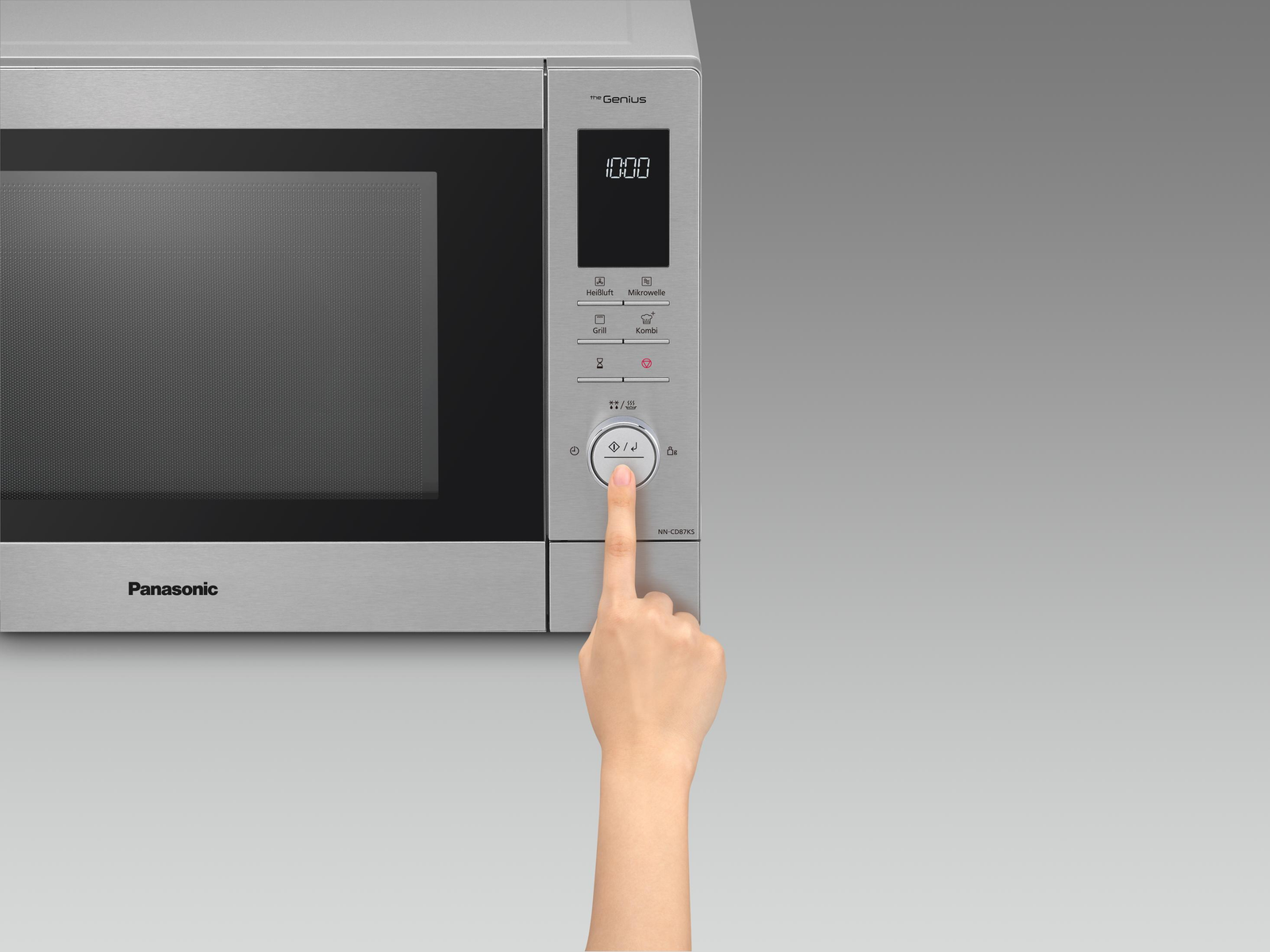 Eine silberne Mikrowelle mit einer Hand, die einen Knopf drückt. Das Display zeigt 10:00.
