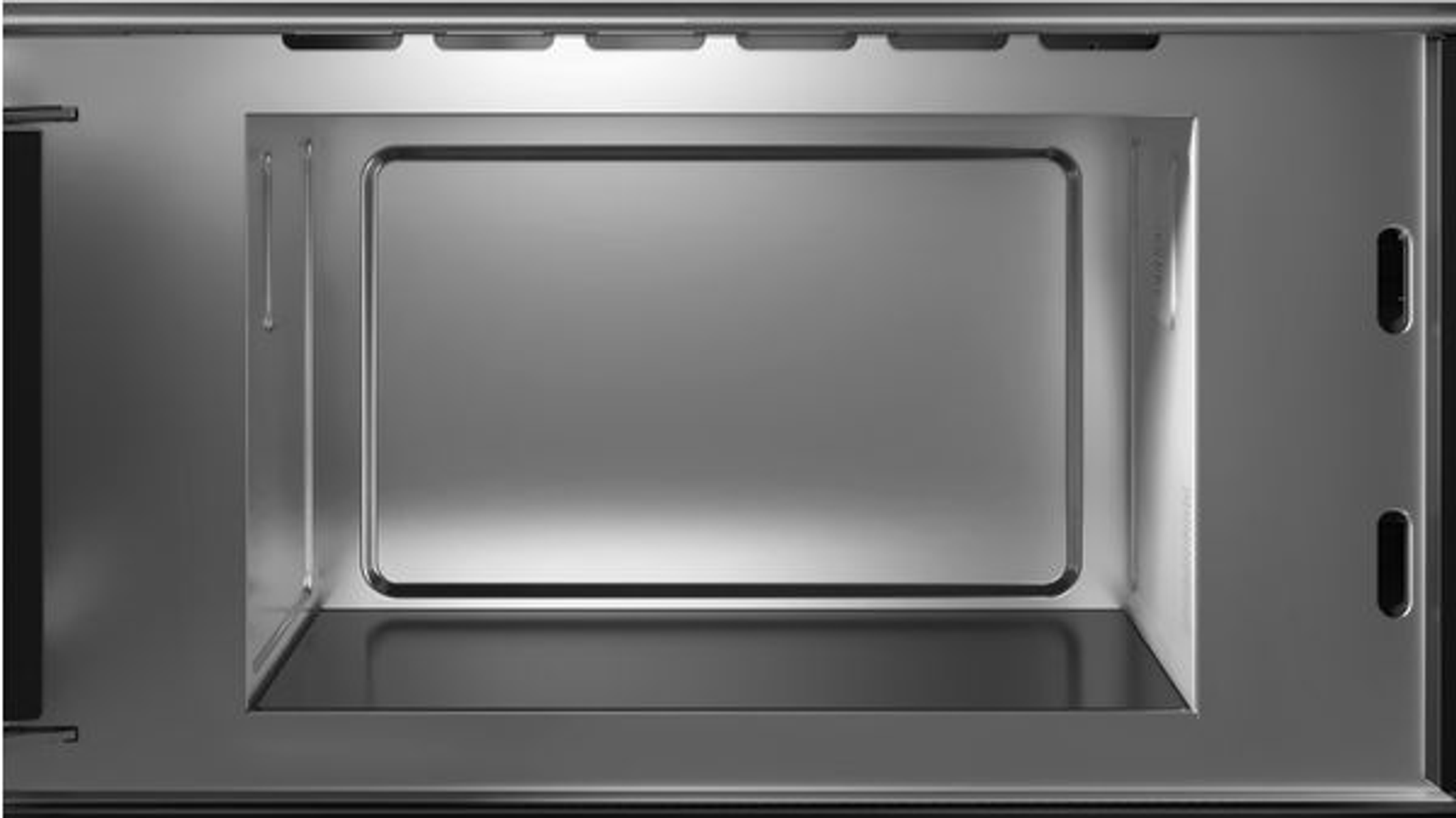 Widok wnętrza błyszczącej, metalicznej wnęki kuchenki mikrofalowej.