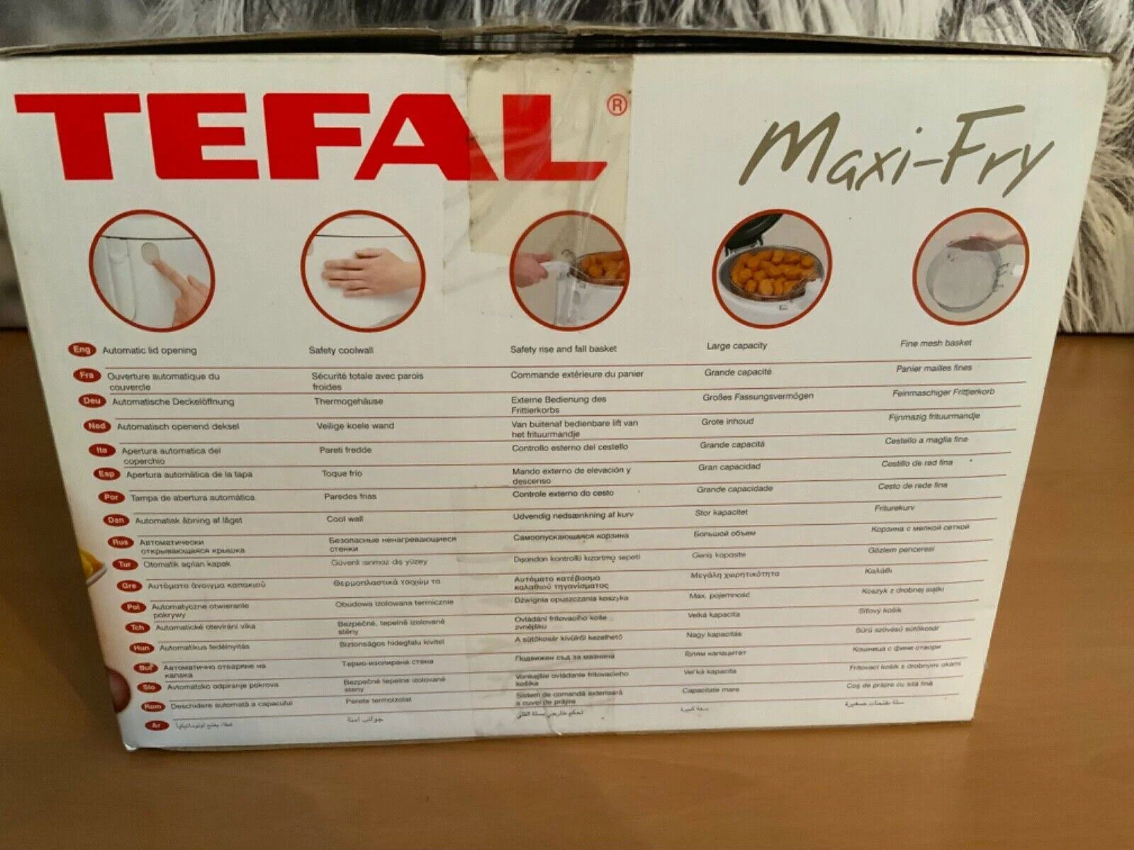Scatola di Tefal Maxi-Fry, con immagini e testo in più lingue, su superficie in legno.
