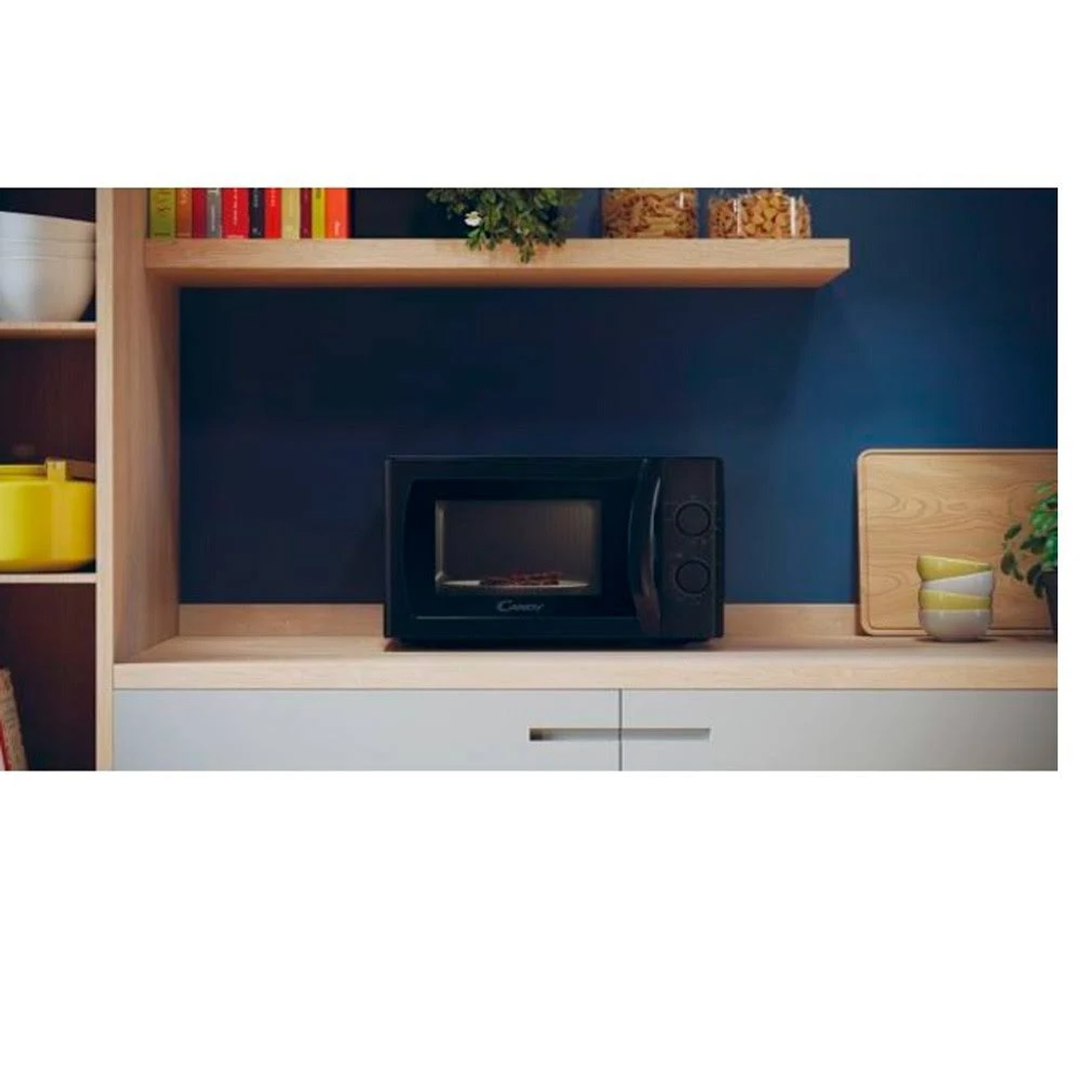 Horno microondas negro en la encimera. Estante de madera, pared azul y decoración en el fondo.