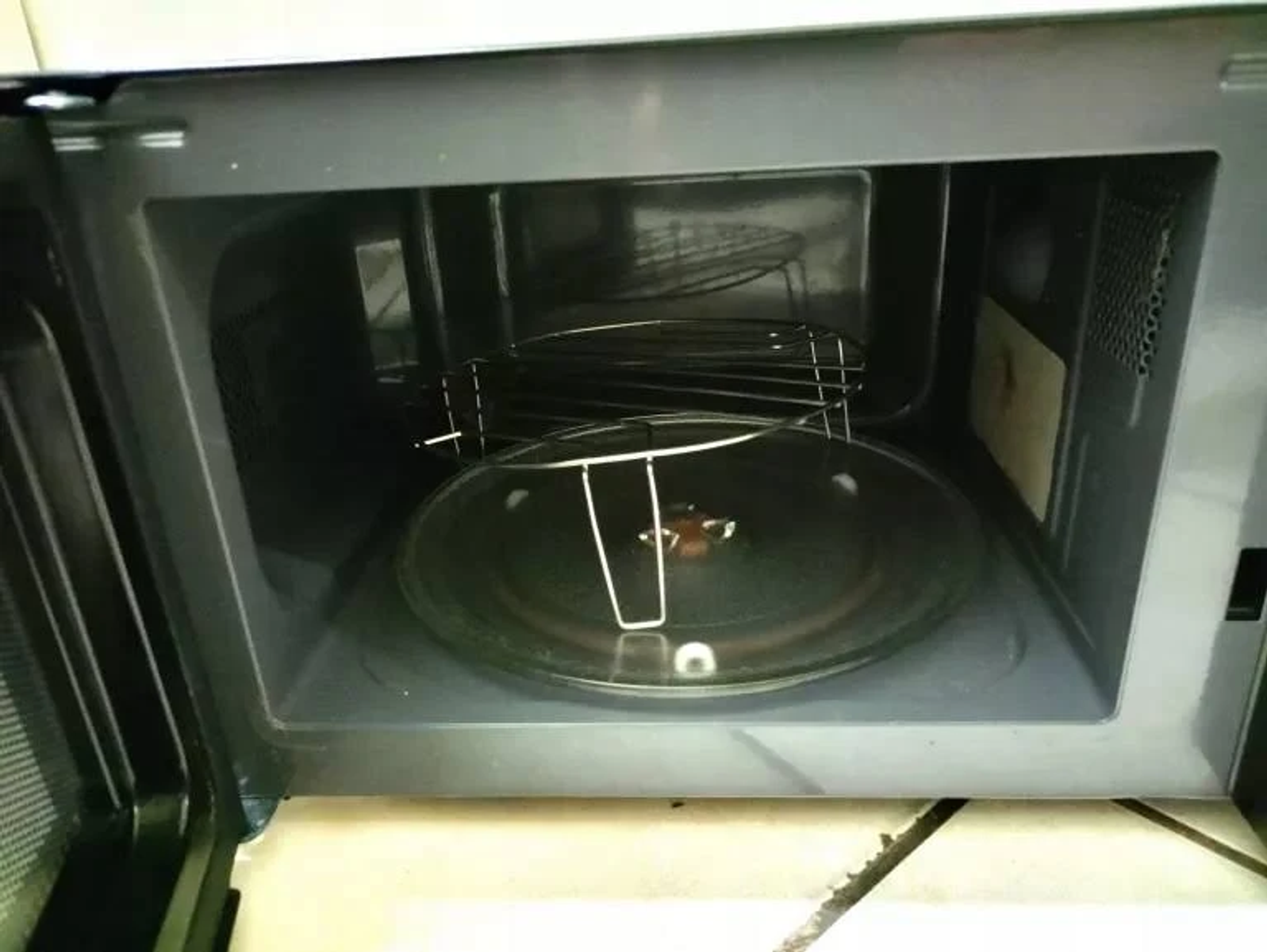 Interior de un horno microondas negro. Tiene un plato de cristal, una rejilla metálica y una luz en el interior.
