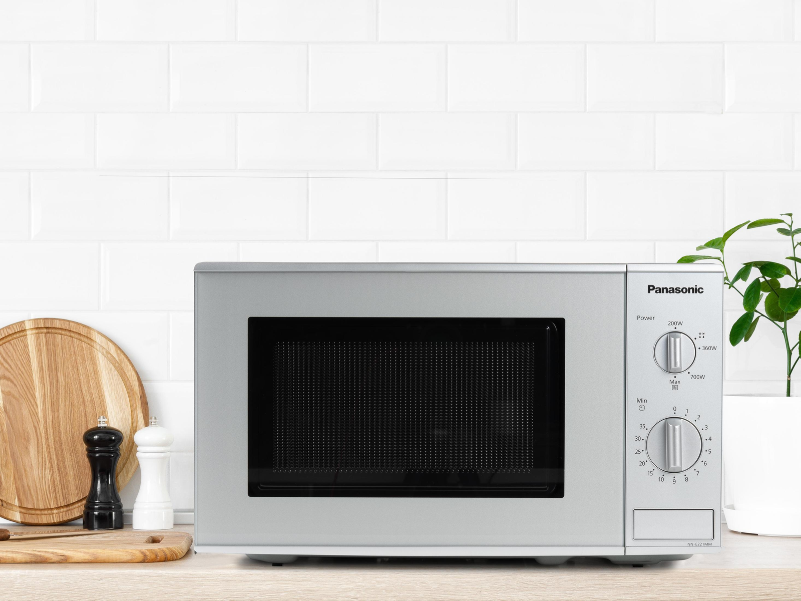 Srebrna kuchenka mikrofalowa na drewnianym blacie. Deska do krojenia po lewej.