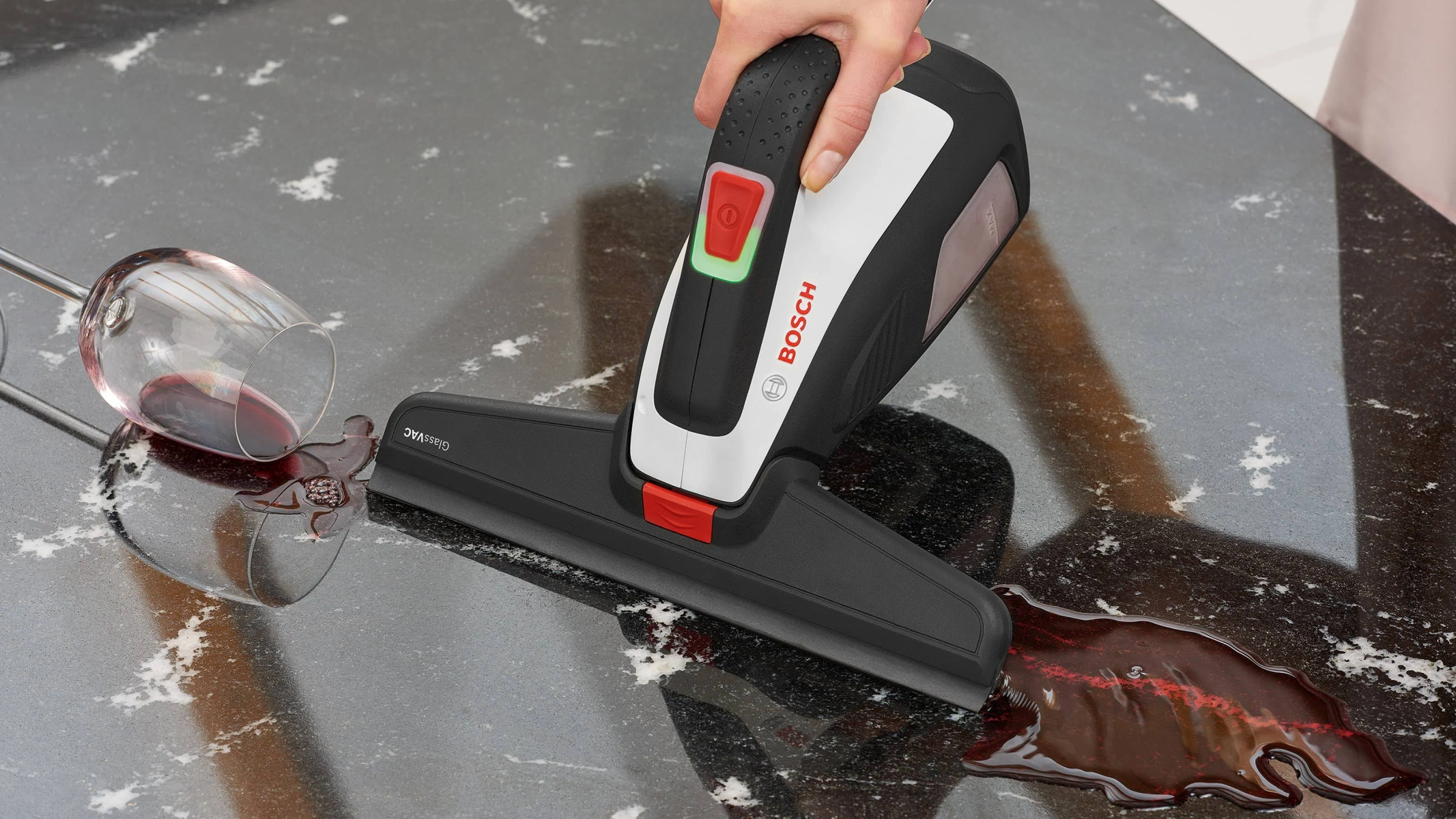 Ręka używająca odkurzacza Bosch do czyszczenia plam z czerwonego wina na czarnej powierzchni.