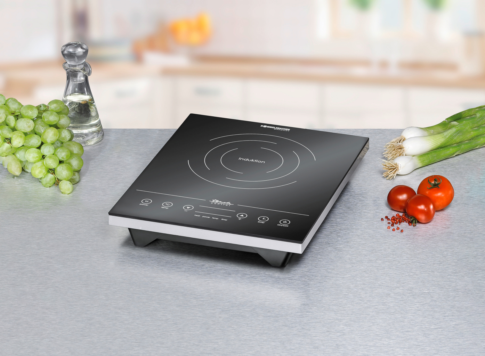 Czarna płyta indukcyjna na metalowej powierzchni. Winogrona, pomidory i dymka w pobliżu.