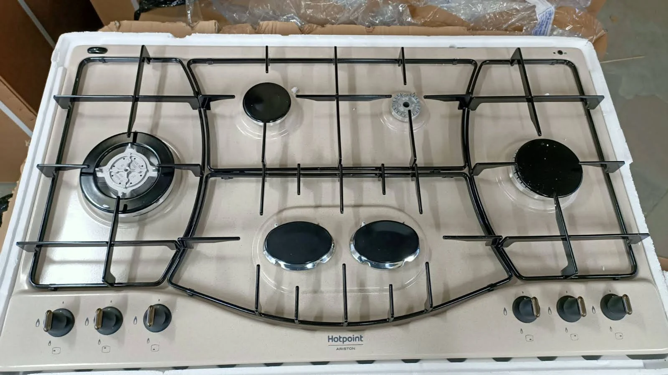 Un piano cottura a gas Hotpoint Ariston beige con cinque bruciatori e griglie nere.