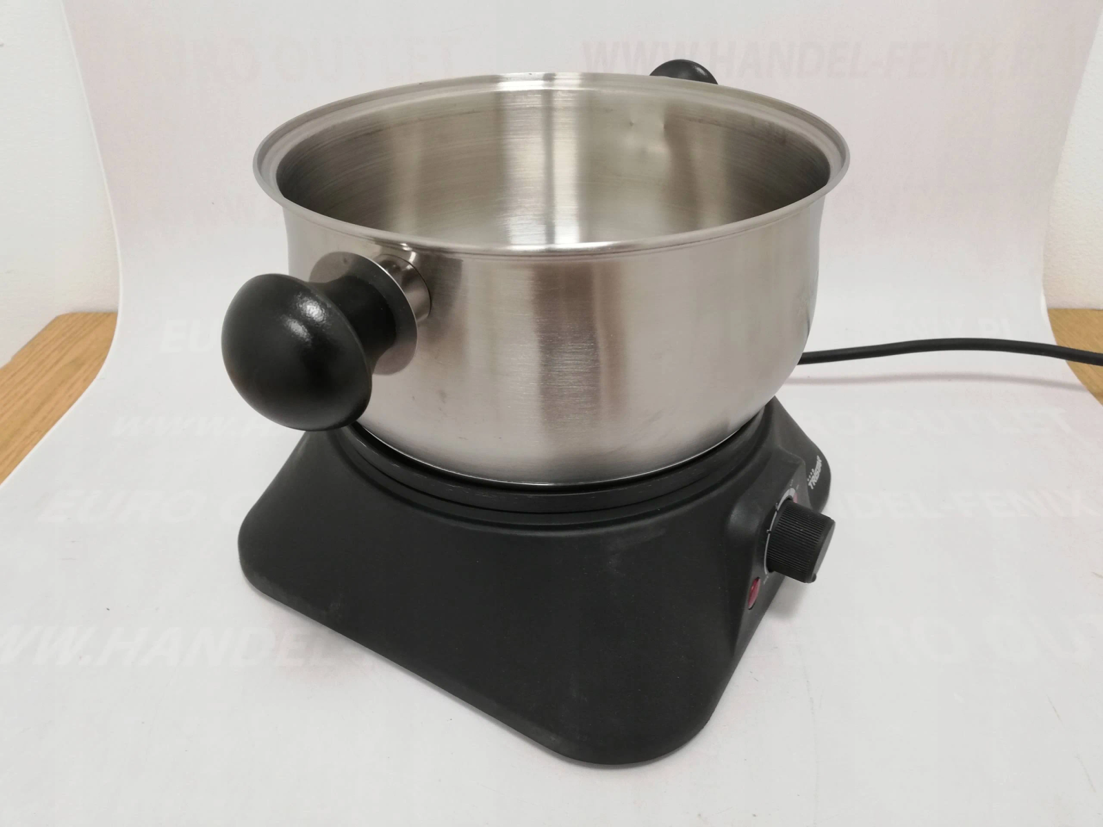 Pentola in acciaio inox su piastra nera. Manici neri. Superficie bianca.