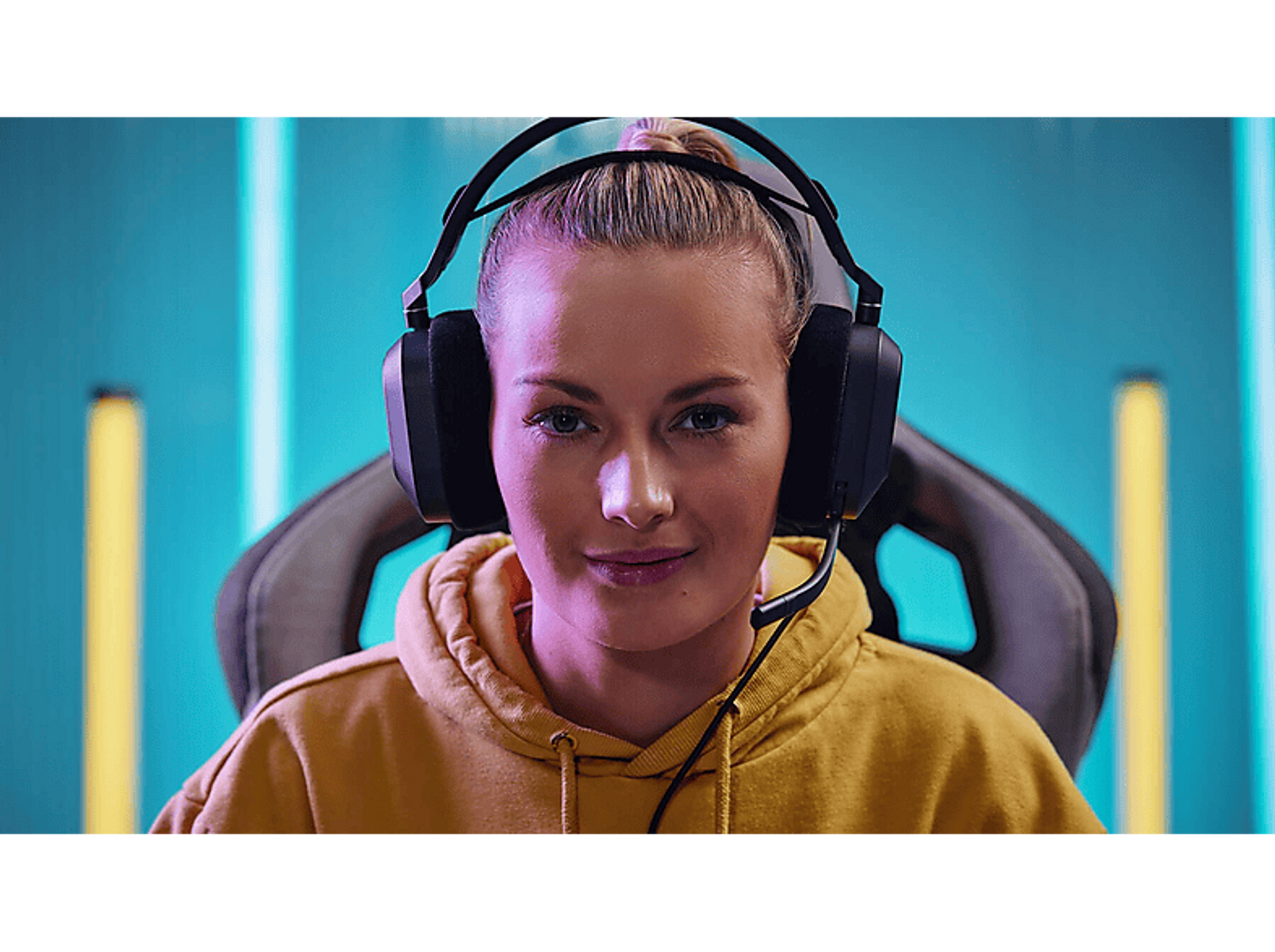 Kobieta w słuchawkach i żółtej bluzie z kapturem, patrząca w kamerę.