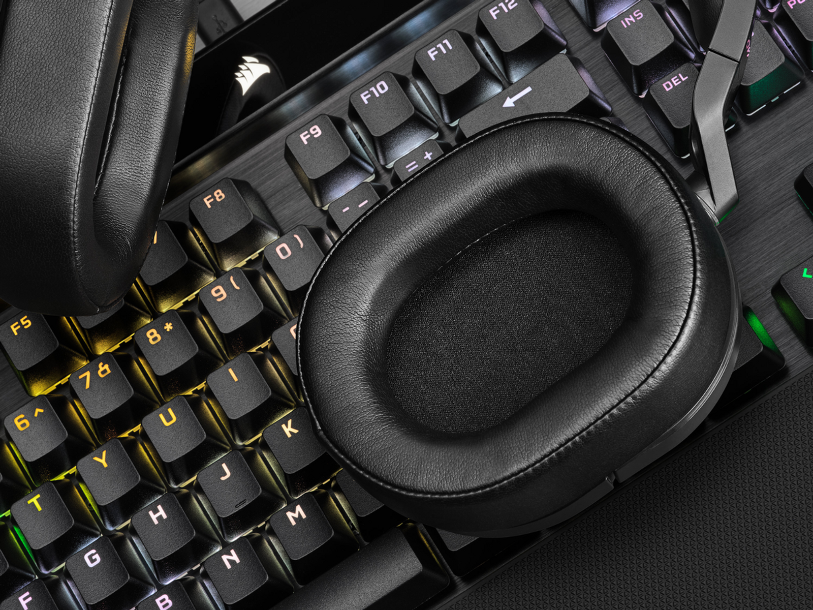 Schwarze Kopfhörer und eine Tastatur. Die Tastatur ist mit bunten Lichtern beleuchtet.