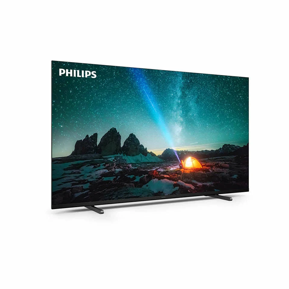 Duży telewizor Philips wyświetla scenę gwiaździstej nocy z namiotem i ogniem. Telewizor stoi na białej ścianie.