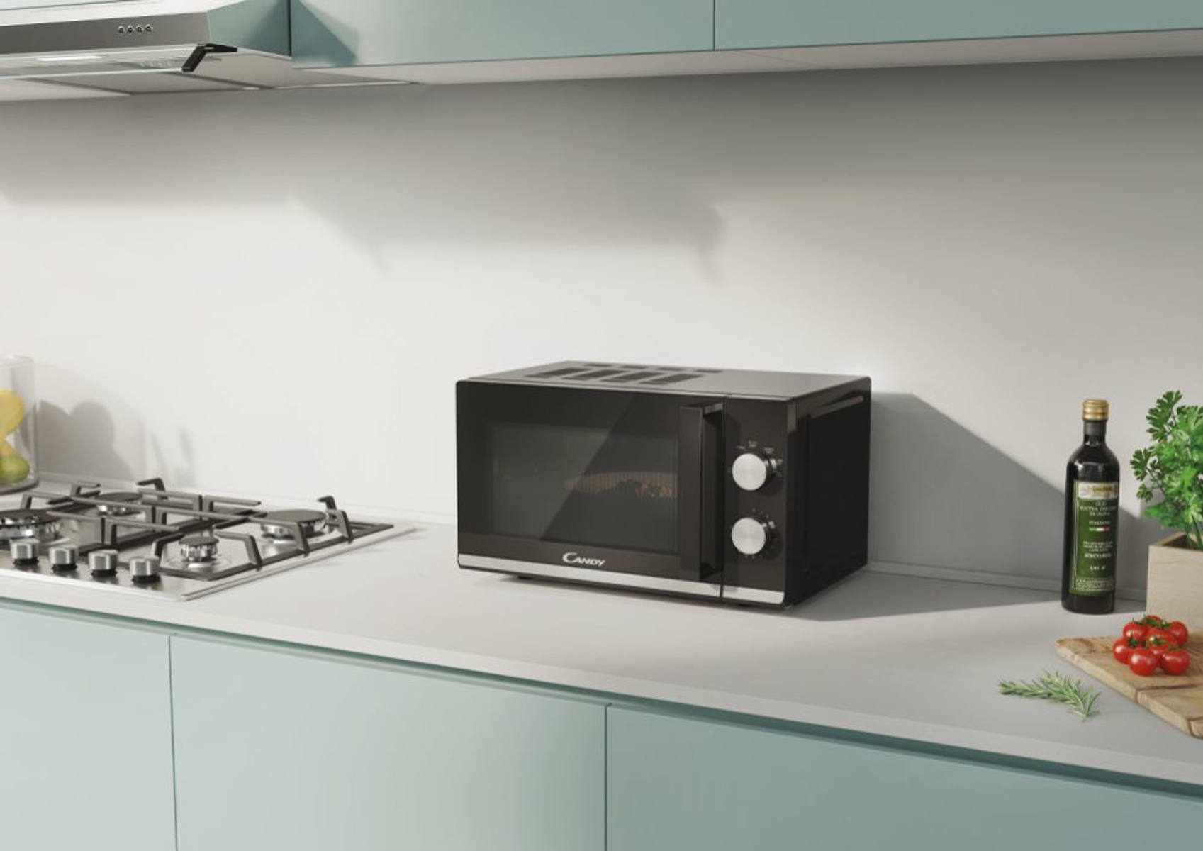 Czarna kuchenka mikrofalowa na białym blacie. W pobliżu kuchenka gazowa i butelka oliwy z oliwek.