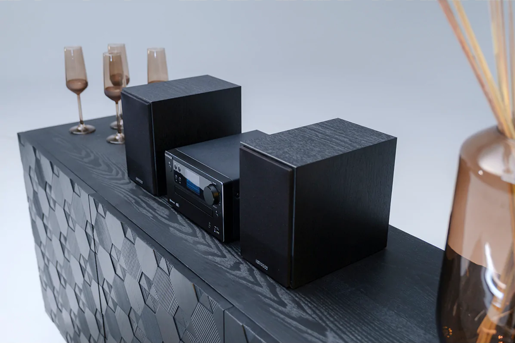 Ein schwarzer Schrank mit Lautsprechern und Stereoanlage, sowie Weingläser und ein Diffusor.