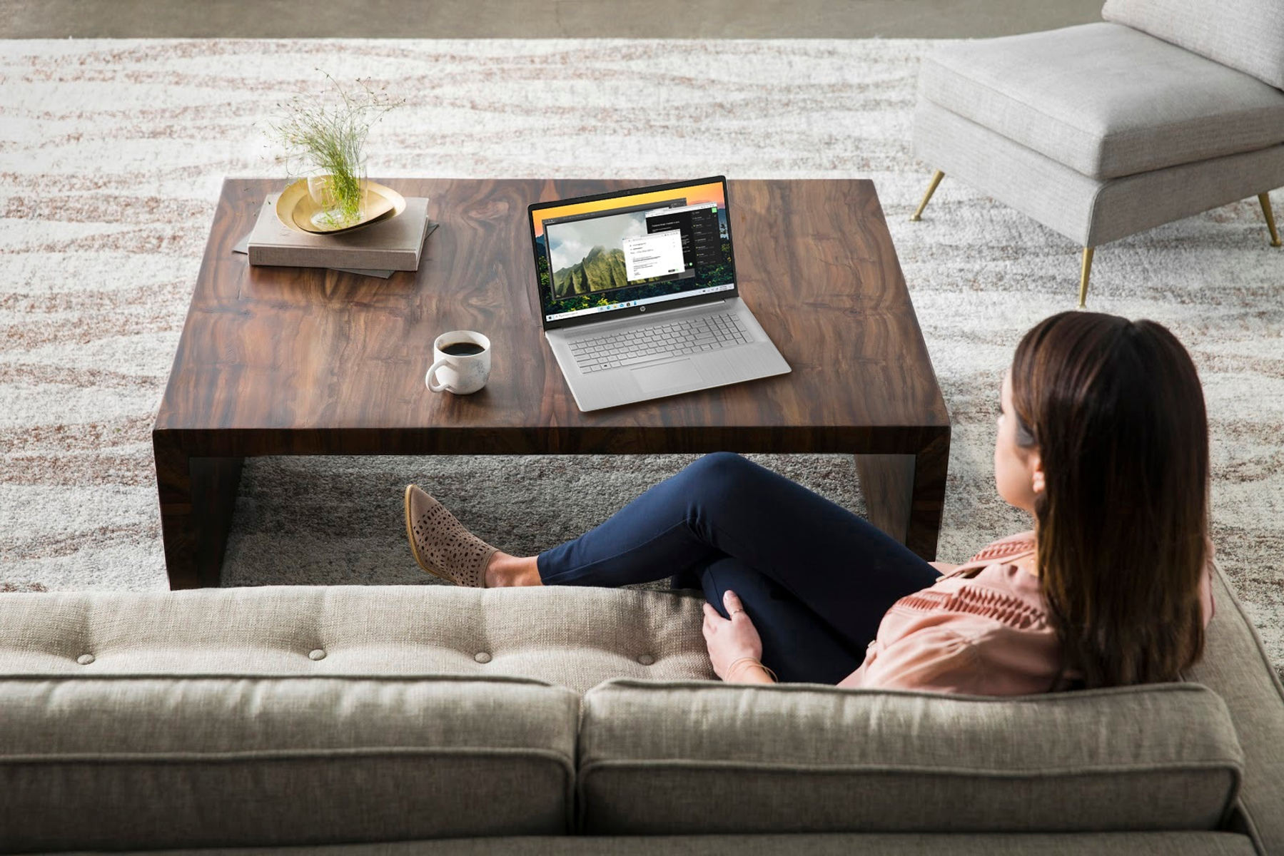 Kobieta na sofie, używająca laptopa na stoliku kawowym. Jasny pokój z rośliną.
