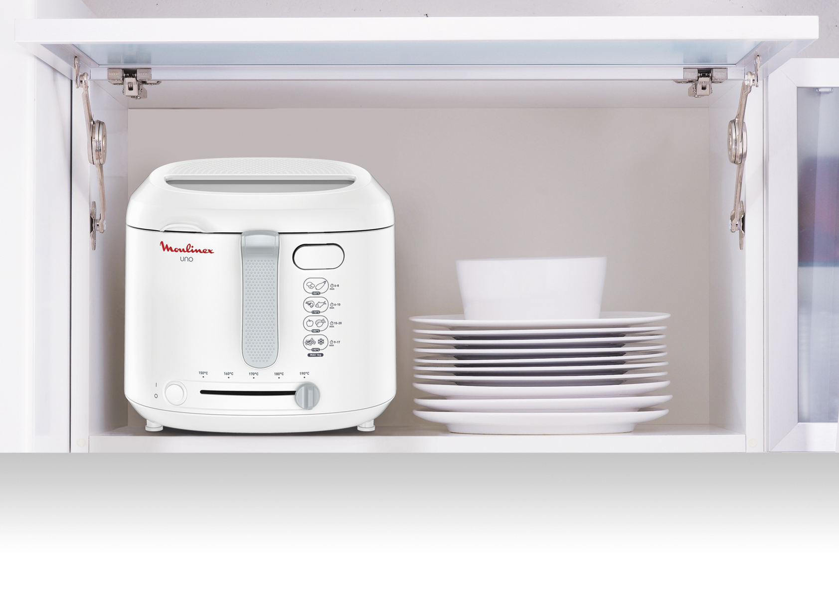 Friteuse blanche dans une armoire ouverte avec des assiettes. Cuisine propre et organisée.