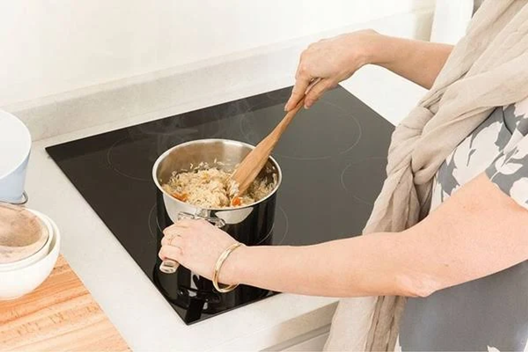 Kobieta miesza jedzenie w garnku na czarnej płycie kuchennej. Garnek paruje.