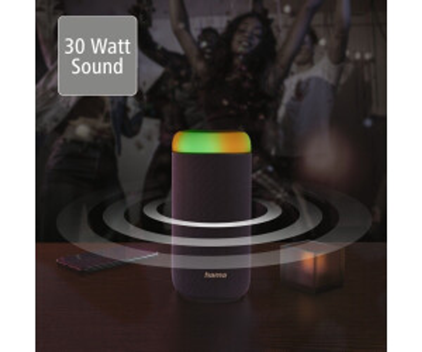 Czarny głośnik z kolorowymi światłami na górze. Grupa ludzi w tle, w ciemności.