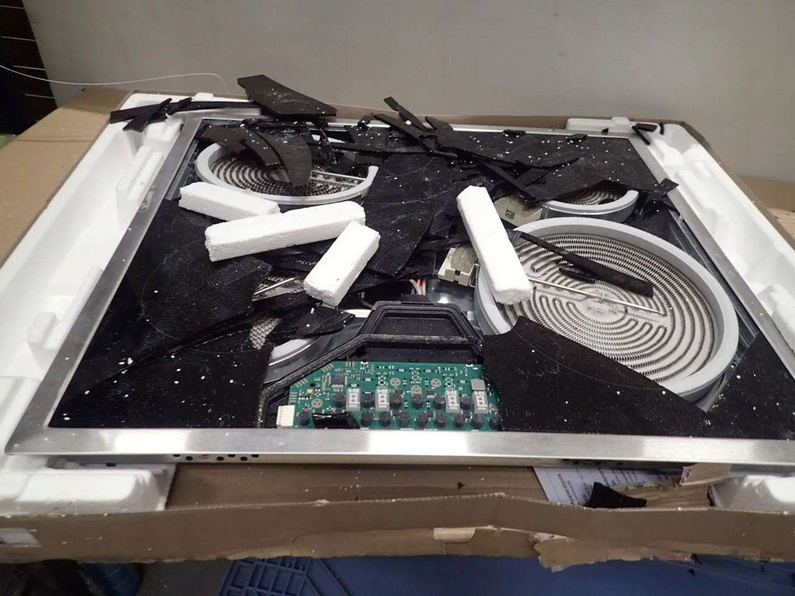 Pęknięta szklana płyta grzejna, ze szklanymi odłamkami i piankowym opakowaniem w pudełku.