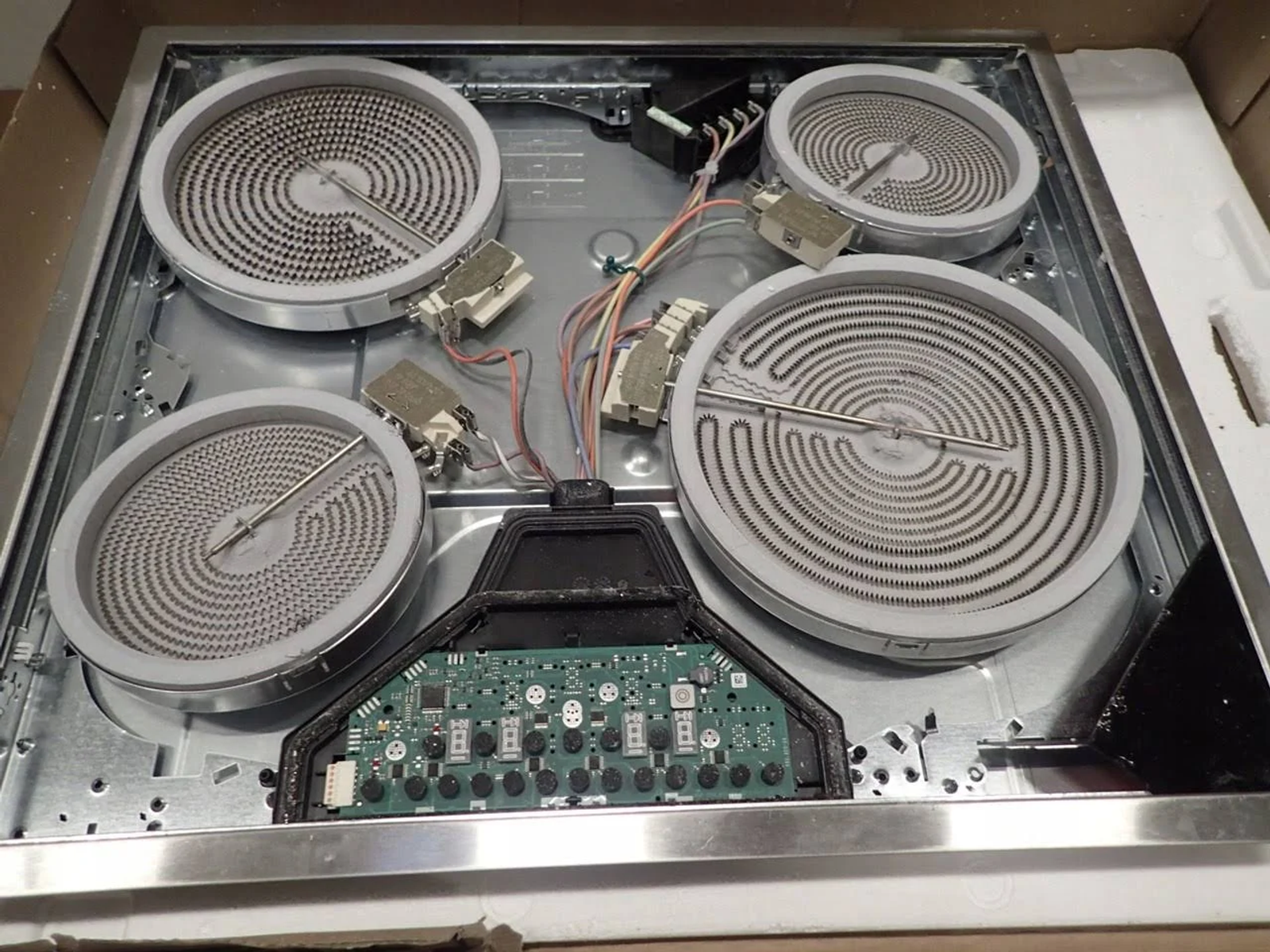 Otwarty elektryczny blat kuchenny z czterema cewkami grzewczymi. Powierzchnia jest metaliczna, a elementy widoczne.