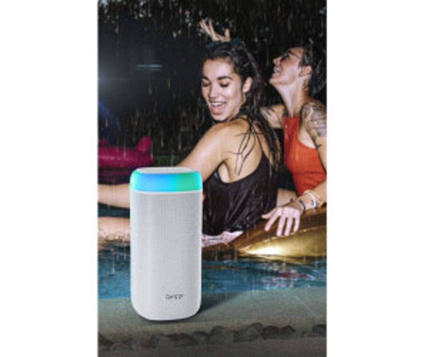 Dwie kobiety bawią się na imprezie przy basenie z białym głośnikiem. Jedna jest w wodzie.