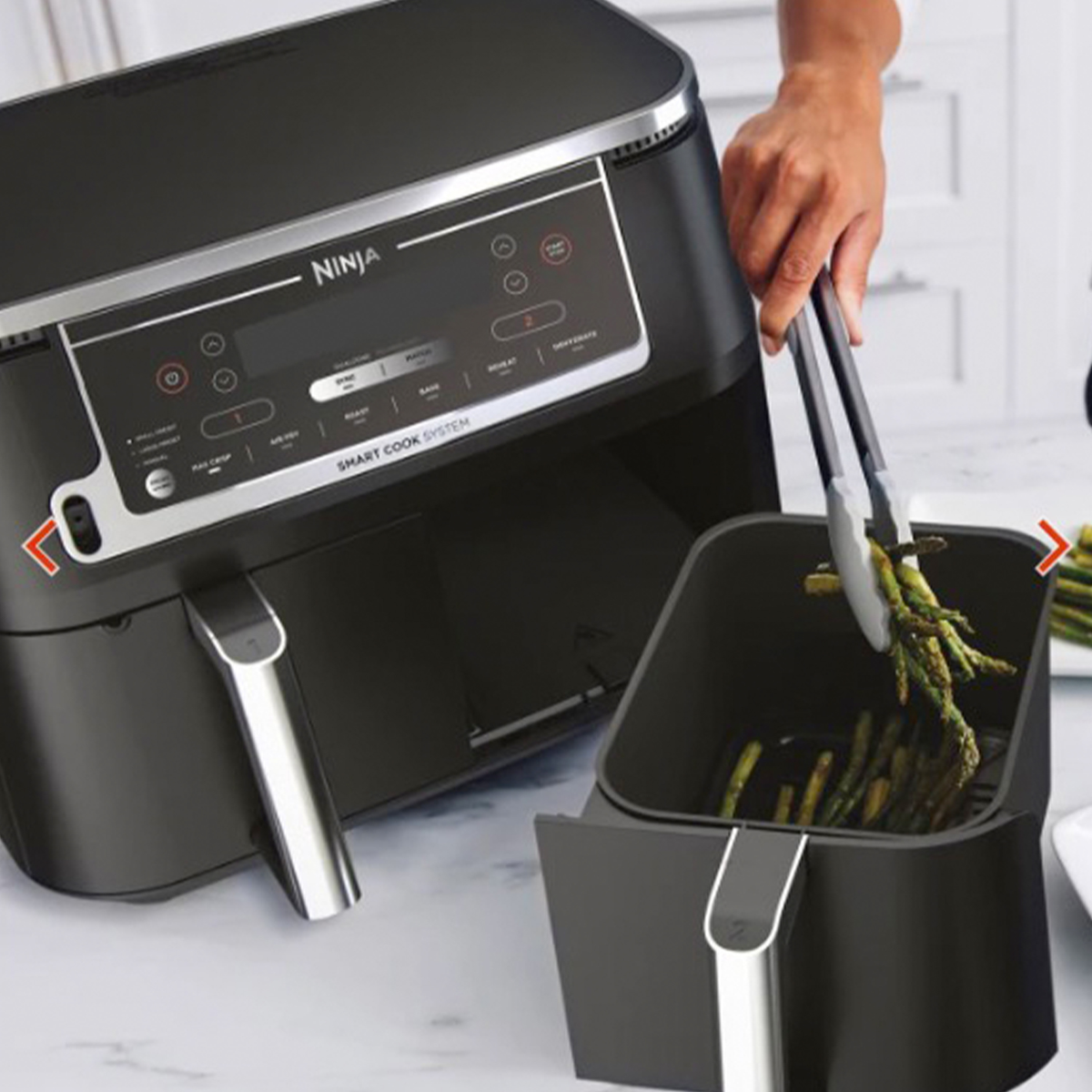 Frytkownica powietrzna ze szparagami wkładanymi do środka za pomocą szczypiec.