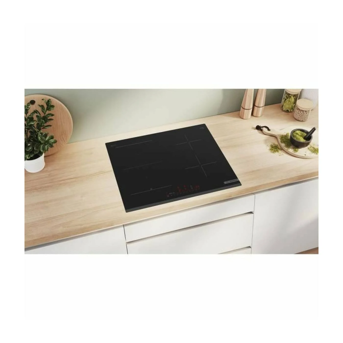 Czarna płyta grzewcza na drewnianej powierzchni z małą rośliną i innymi akcesoriami kuchennymi.
