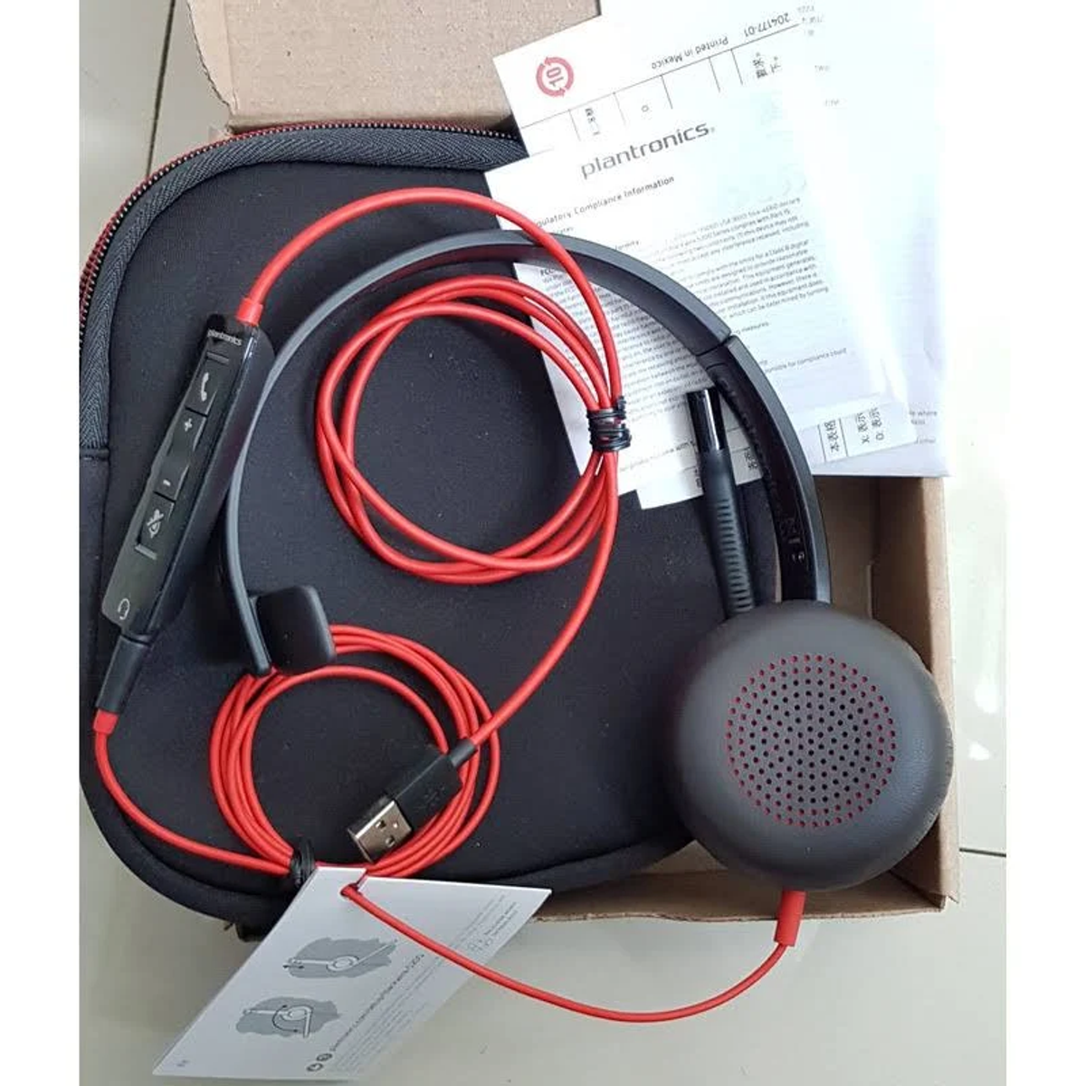 Zestaw słuchawkowy Plantronics z czerwonymi przewodami, czarnym etui i dokumentami w otwartym pudełku.