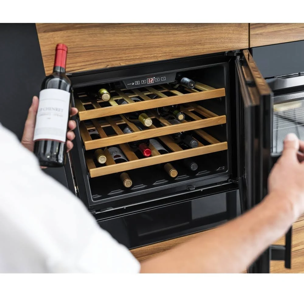 Persona che tiene una bottiglia di vino davanti a una cantina.