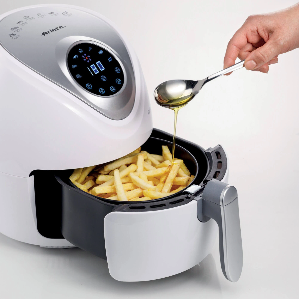 Una friggitrice ad aria con patatine fritte all'interno, viene versato olio.