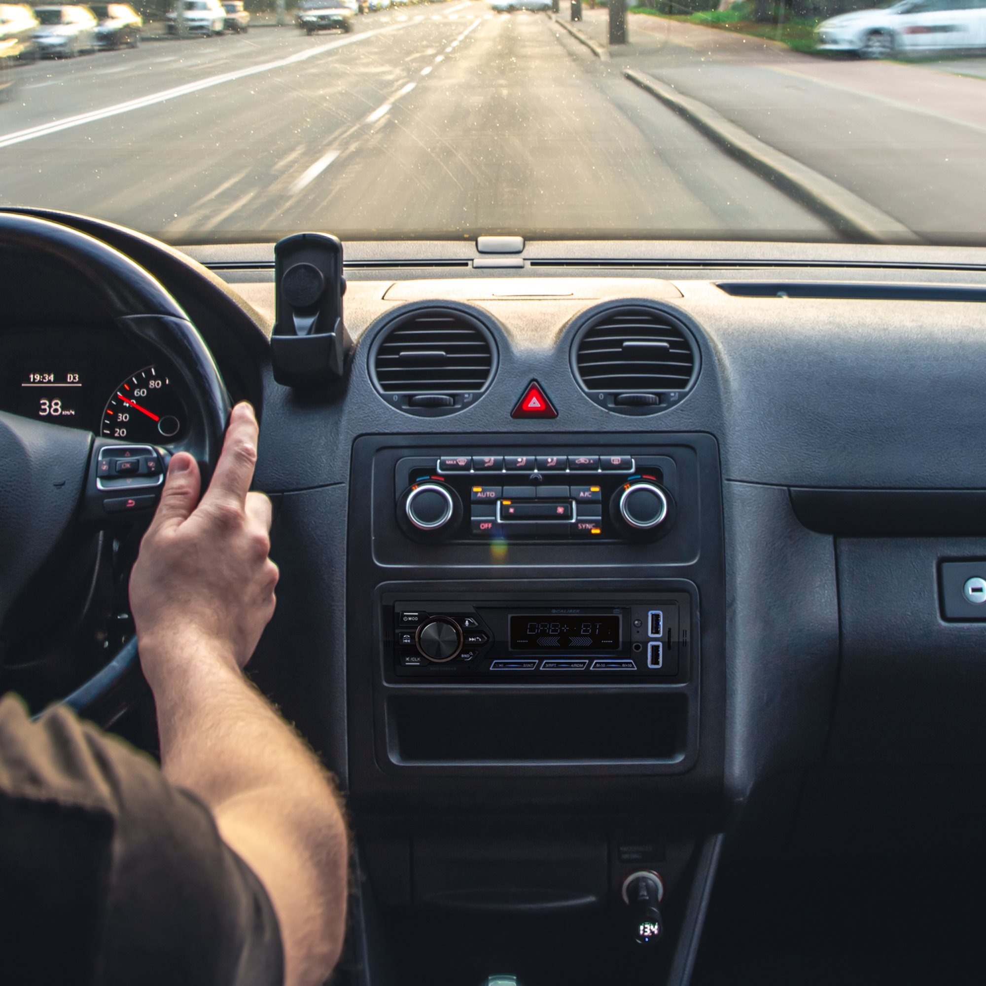 Ansicht des Armaturenbretts im Auto, mit Hand am Lenkrad und Radio.