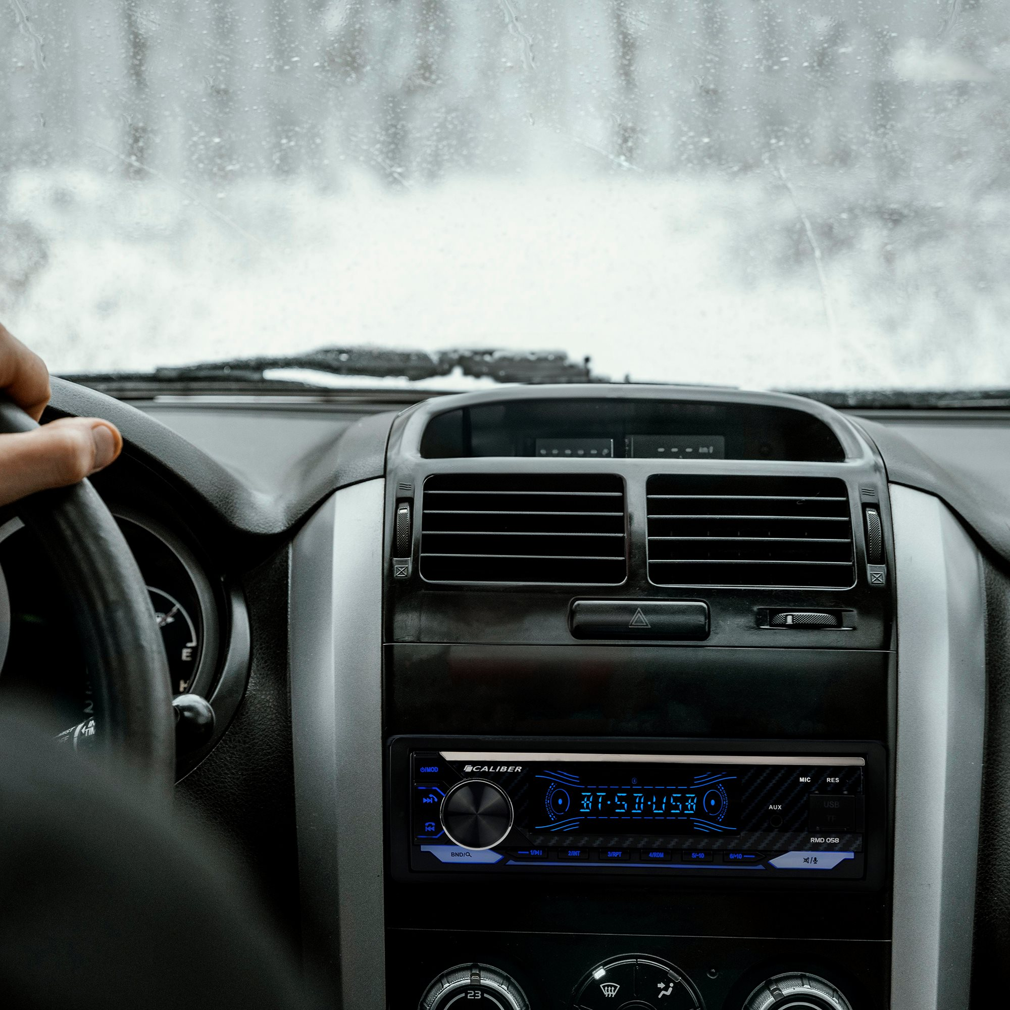 Innenaufnahme eines Autos. Eine Hand am Lenkrad und ein Autoradio mit Digitalanzeige.